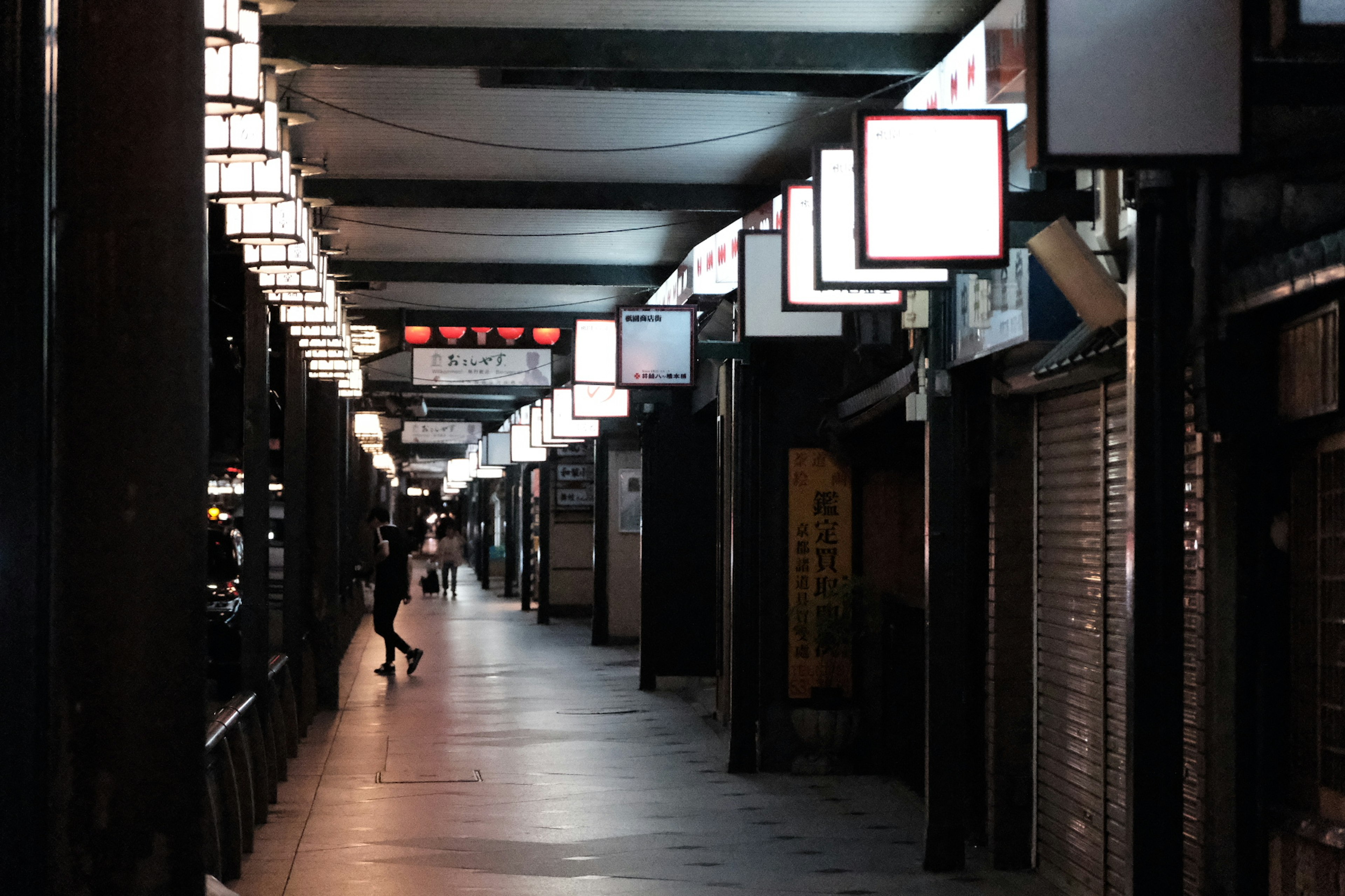 Rue commerçante calme avec des enseignes lumineuses et des volets fermés