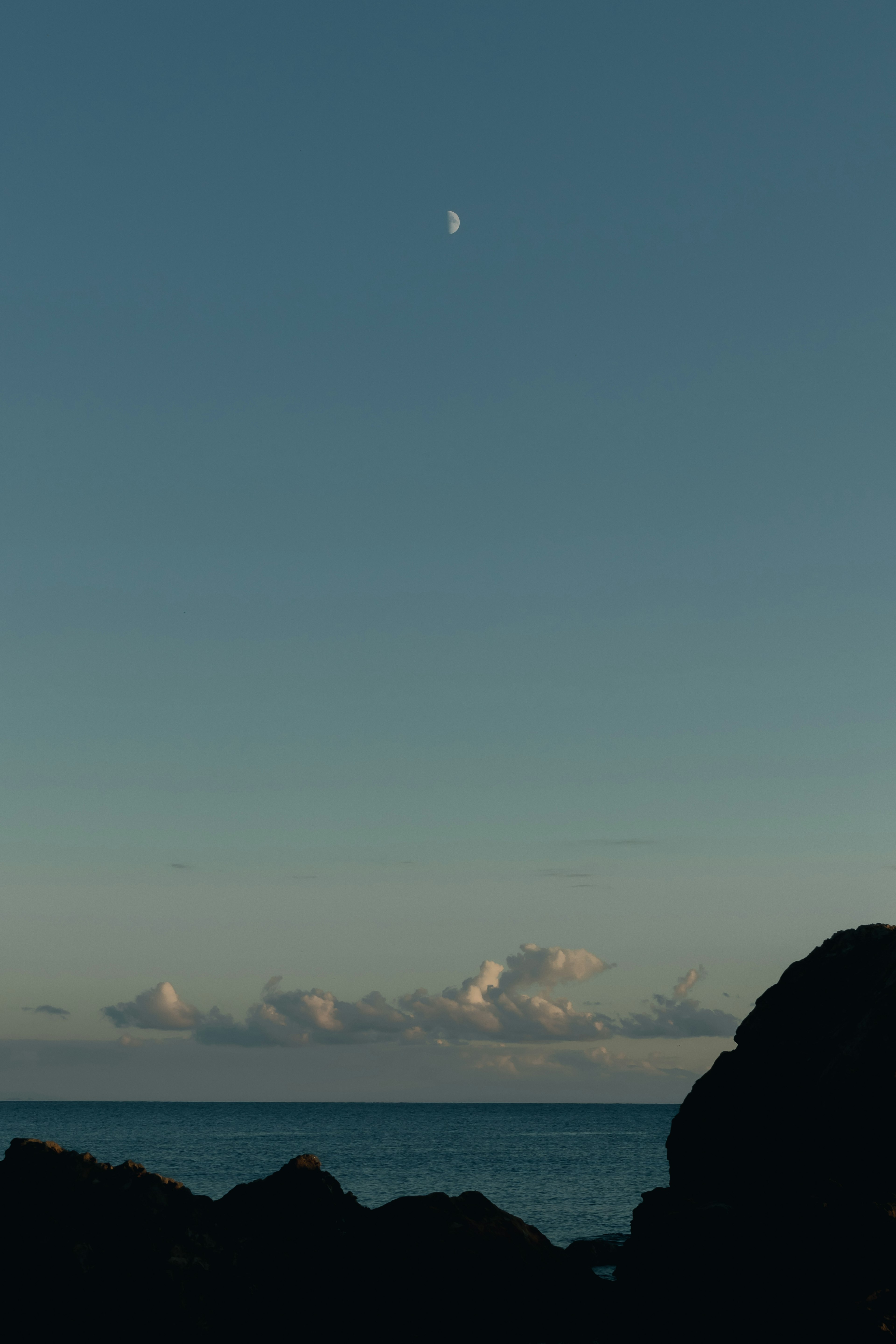 Una escena oceánica serena con una luna creciente y nubes suaves en el cielo