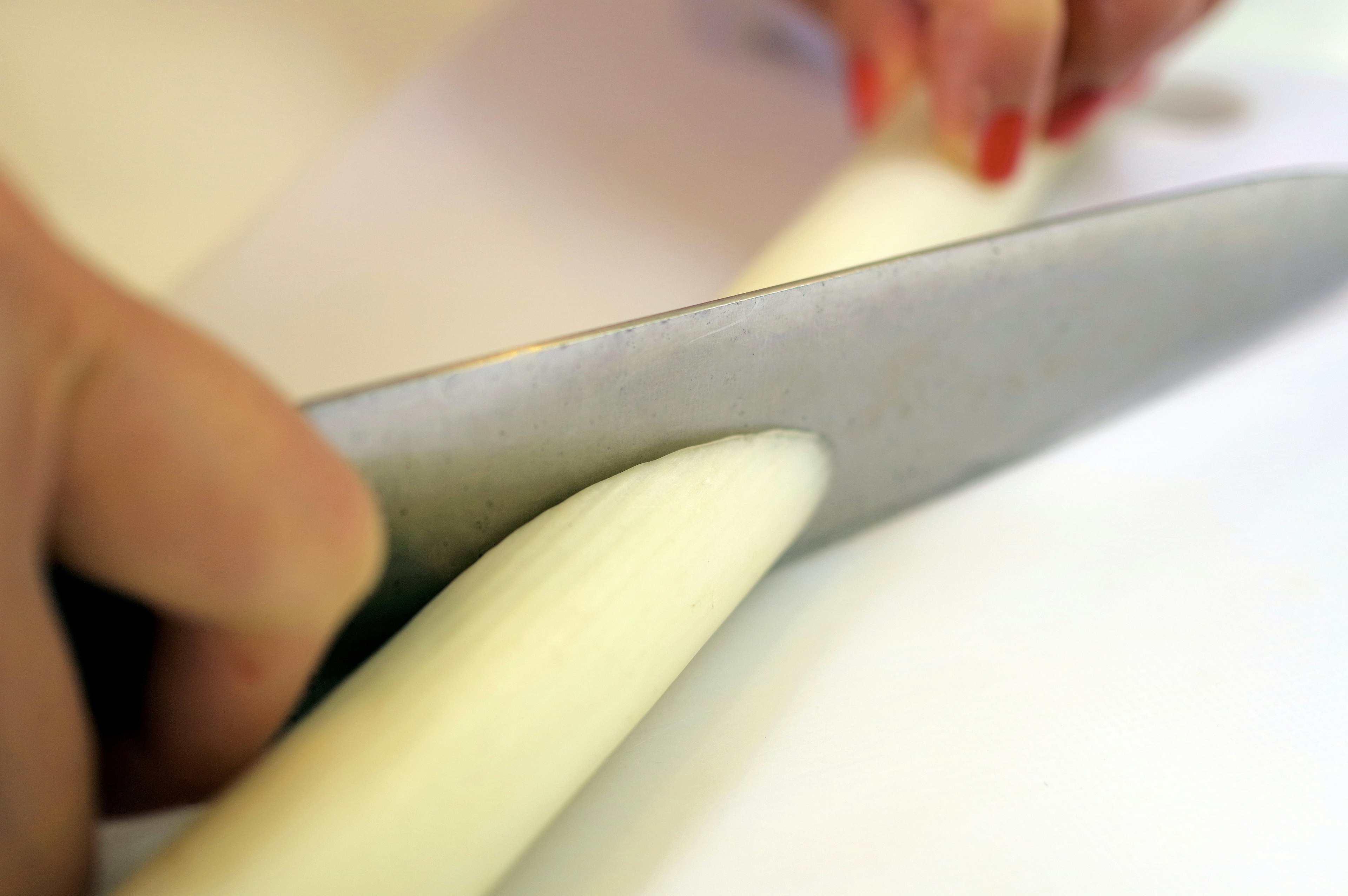 A hand cutting a white vegetable with a knife