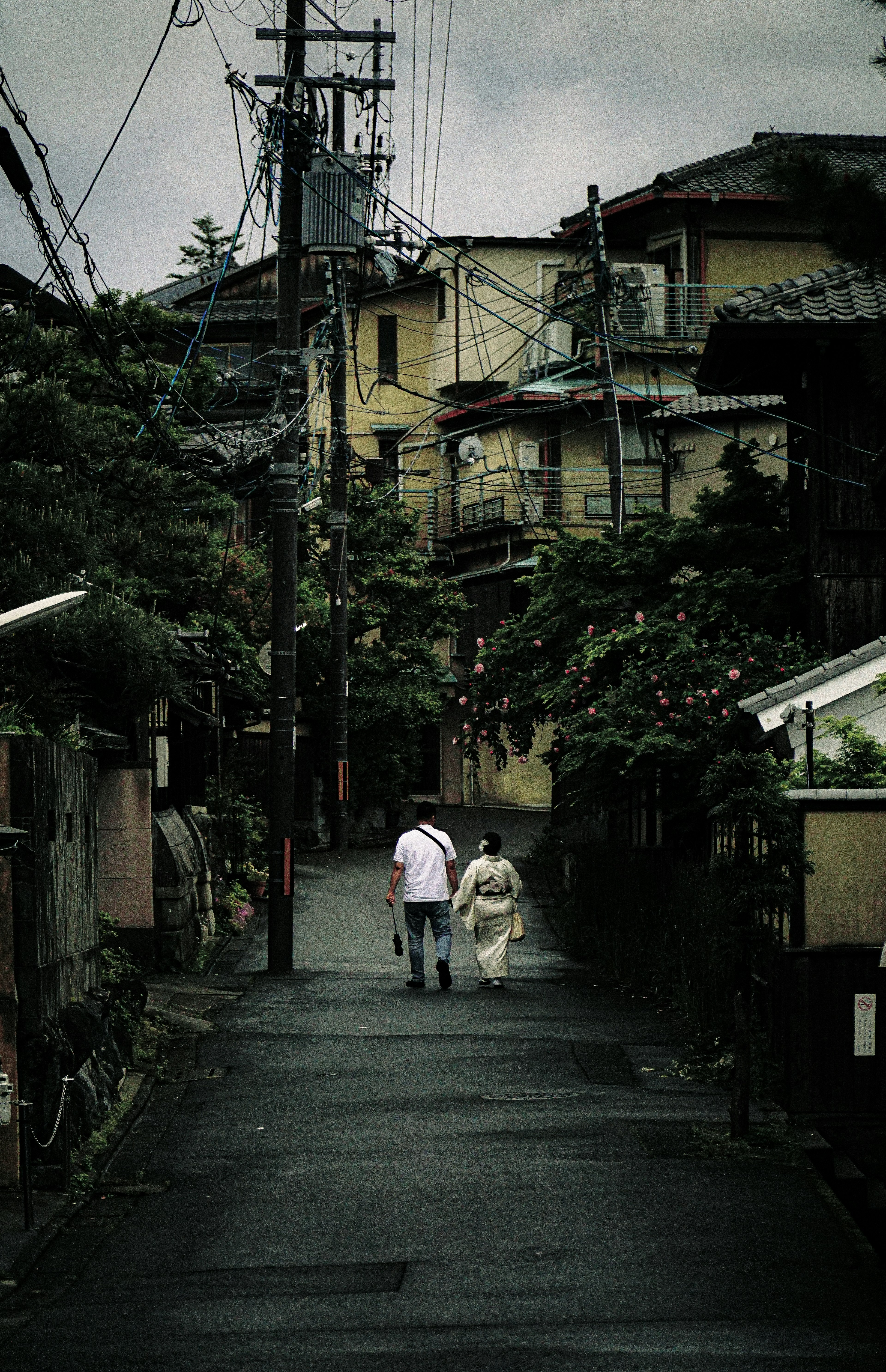 暗い道を歩く二人の人物と古い建物が見える