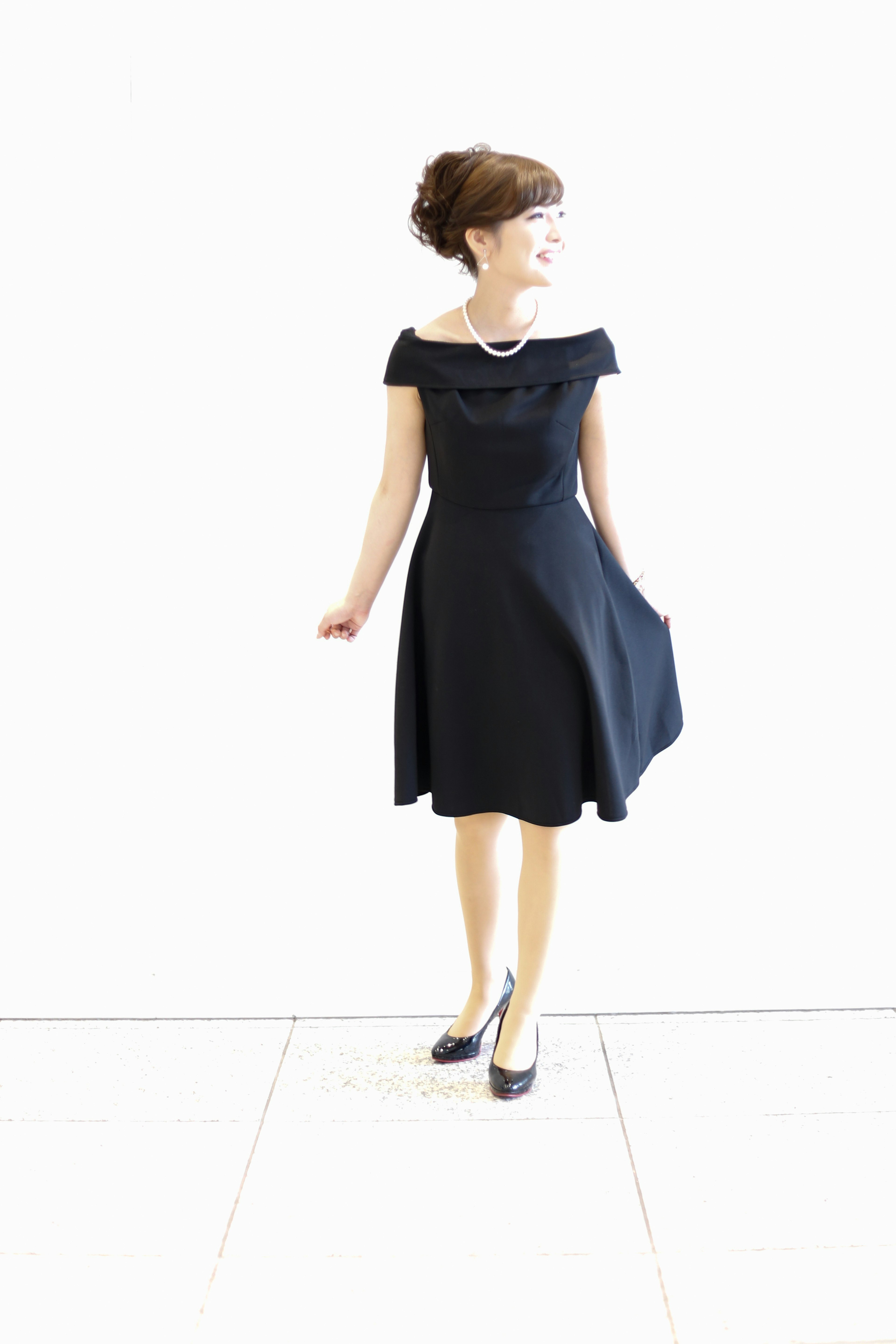 Woman posing in an off-shoulder black dress against a white background