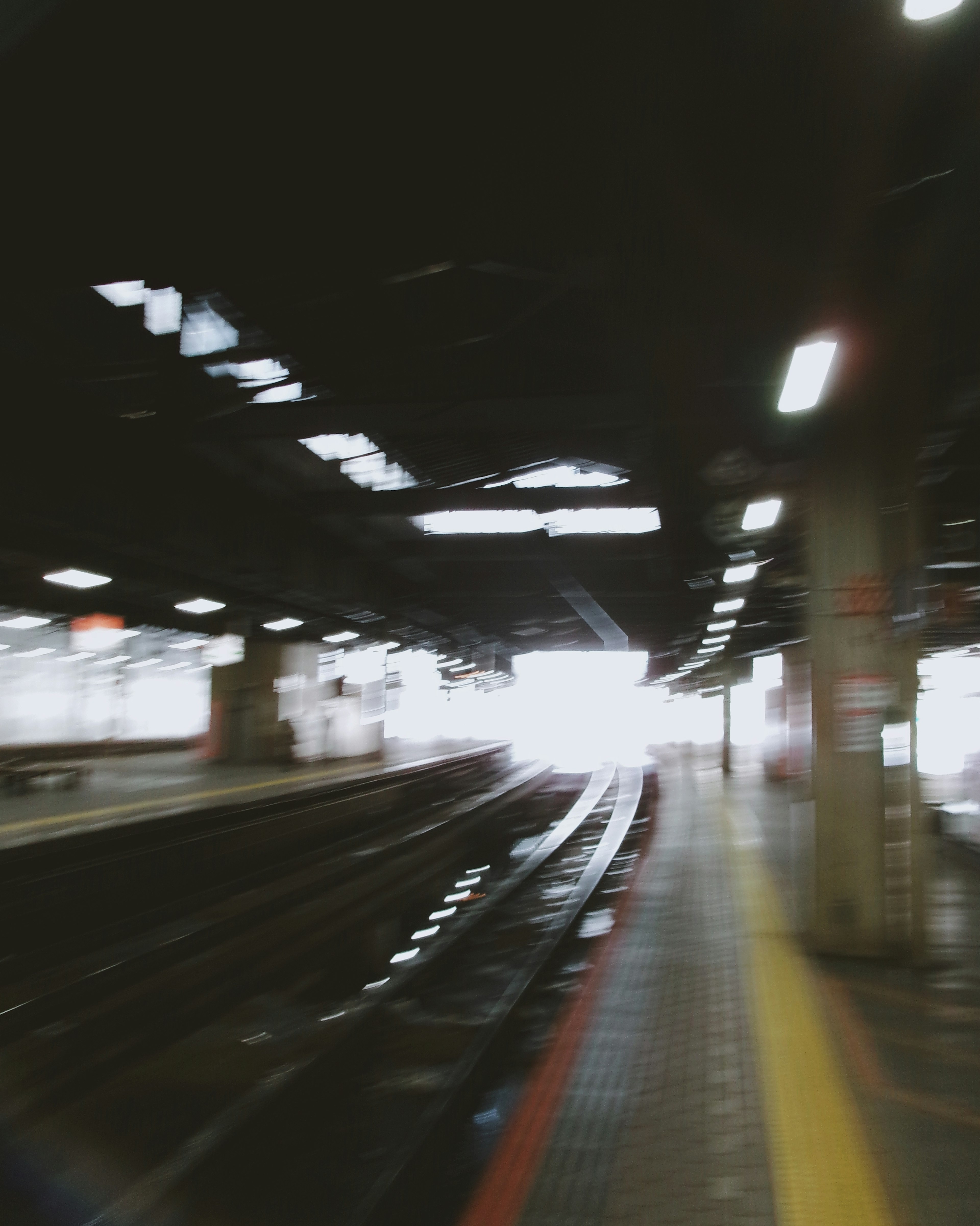 Verschwommene Bild einer Bahnhof-Plattform und Gleise, die zu einem hellen Ausgang führen