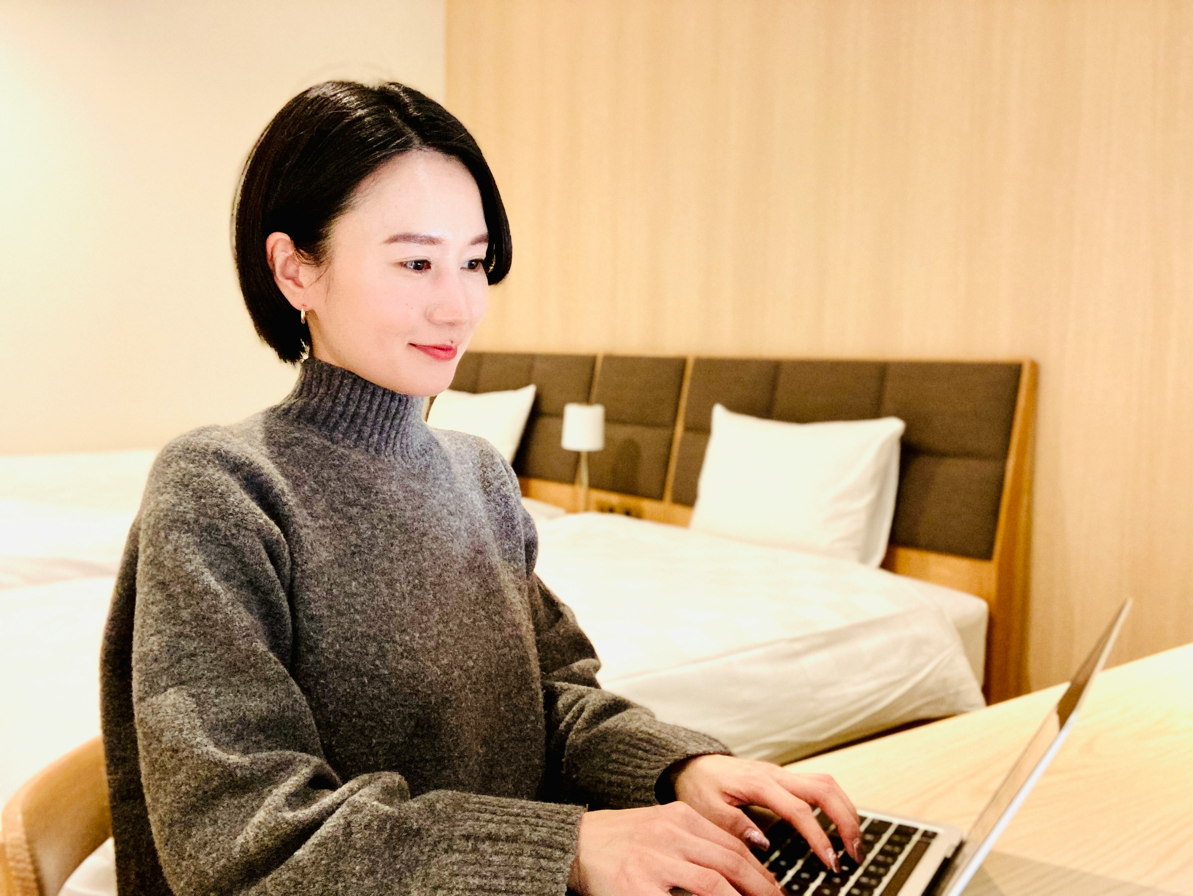 Donna in maglione grigio che lavora al computer portatile in una camera d'hotel