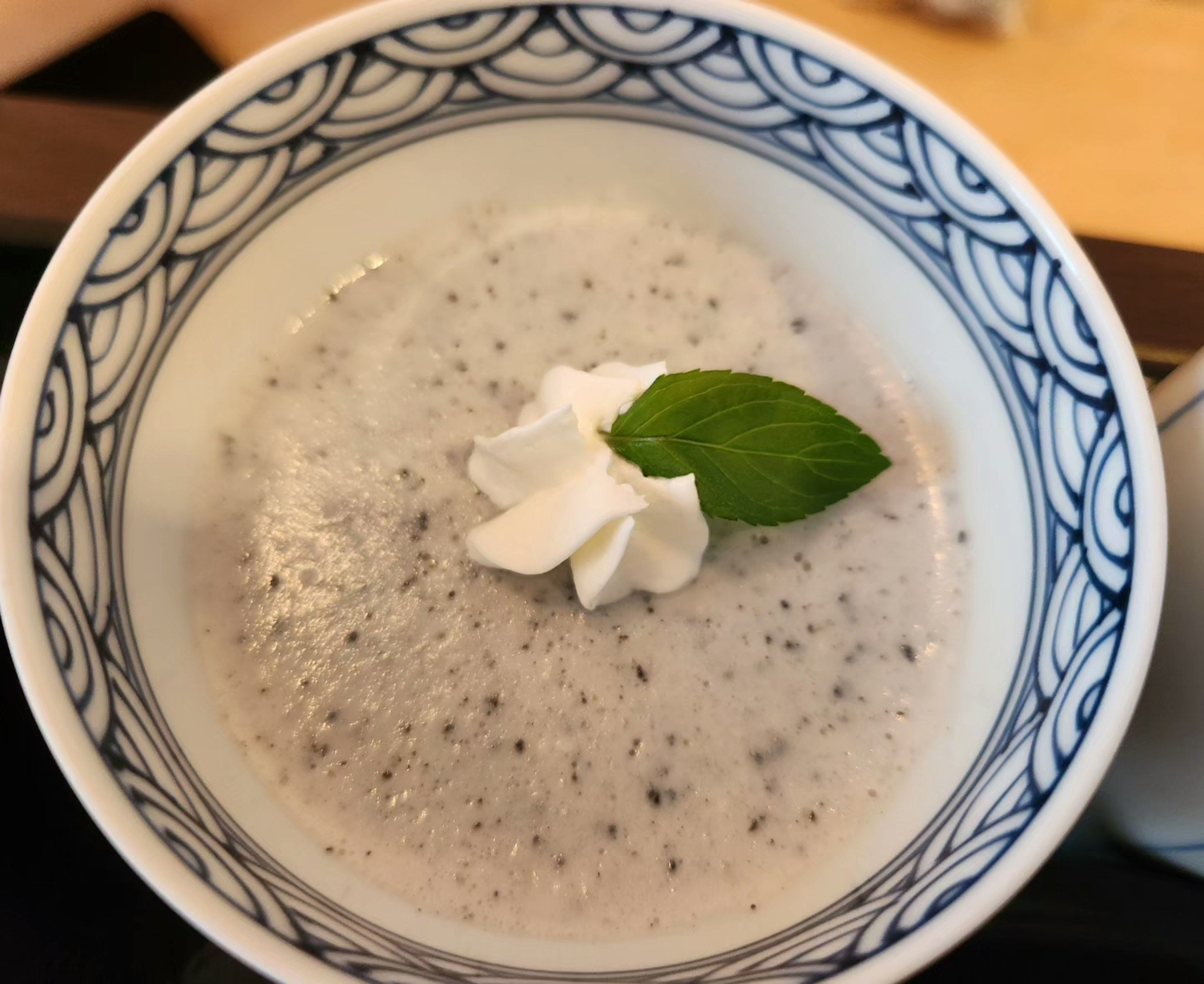 Creamy white dessert topped with mint leaf and whipped cream in a Japanese-style bowl