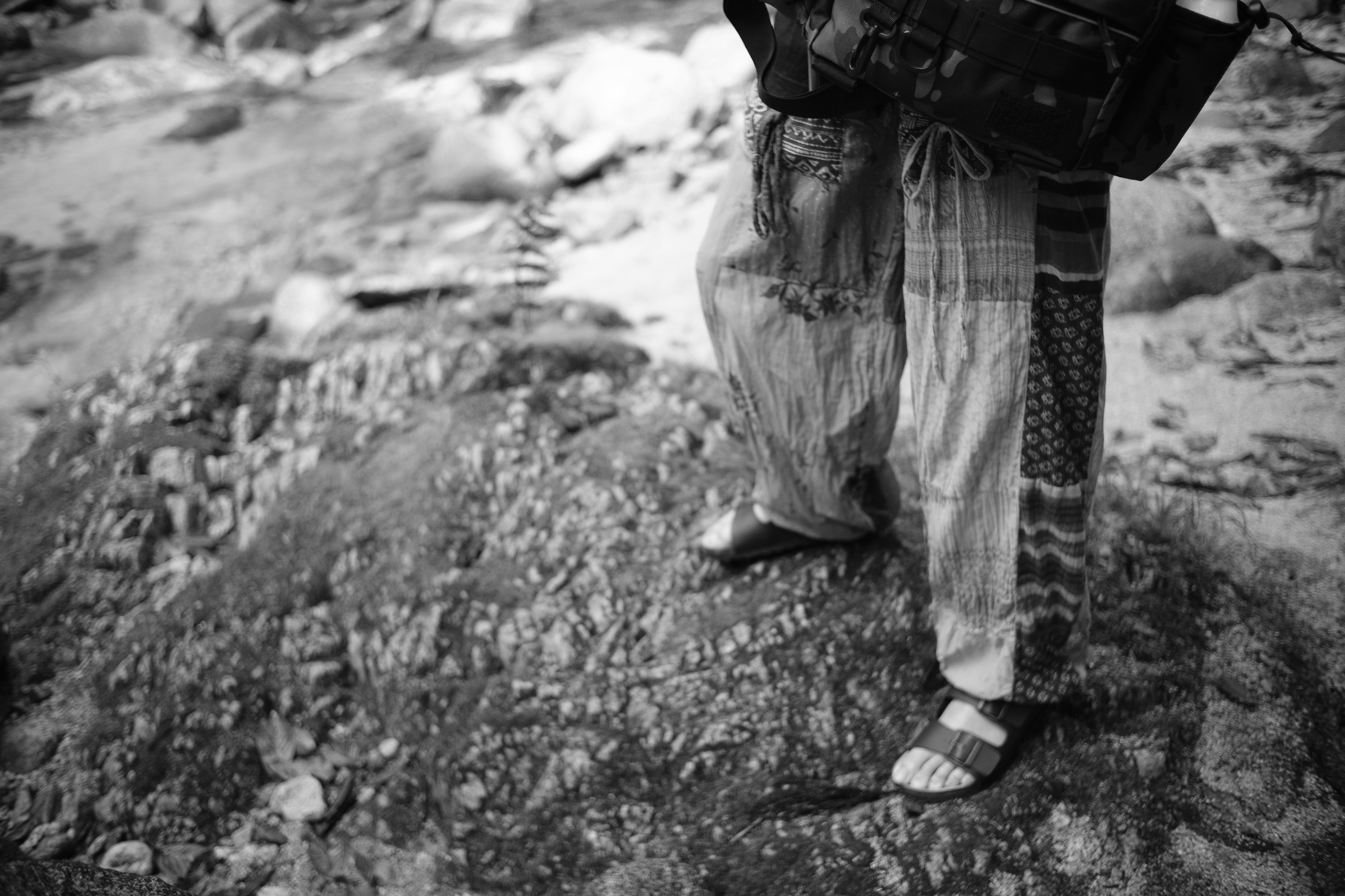 Photo en noir et blanc d'une personne debout au bord d'une rivière portant un pantalon à motifs et des sandales