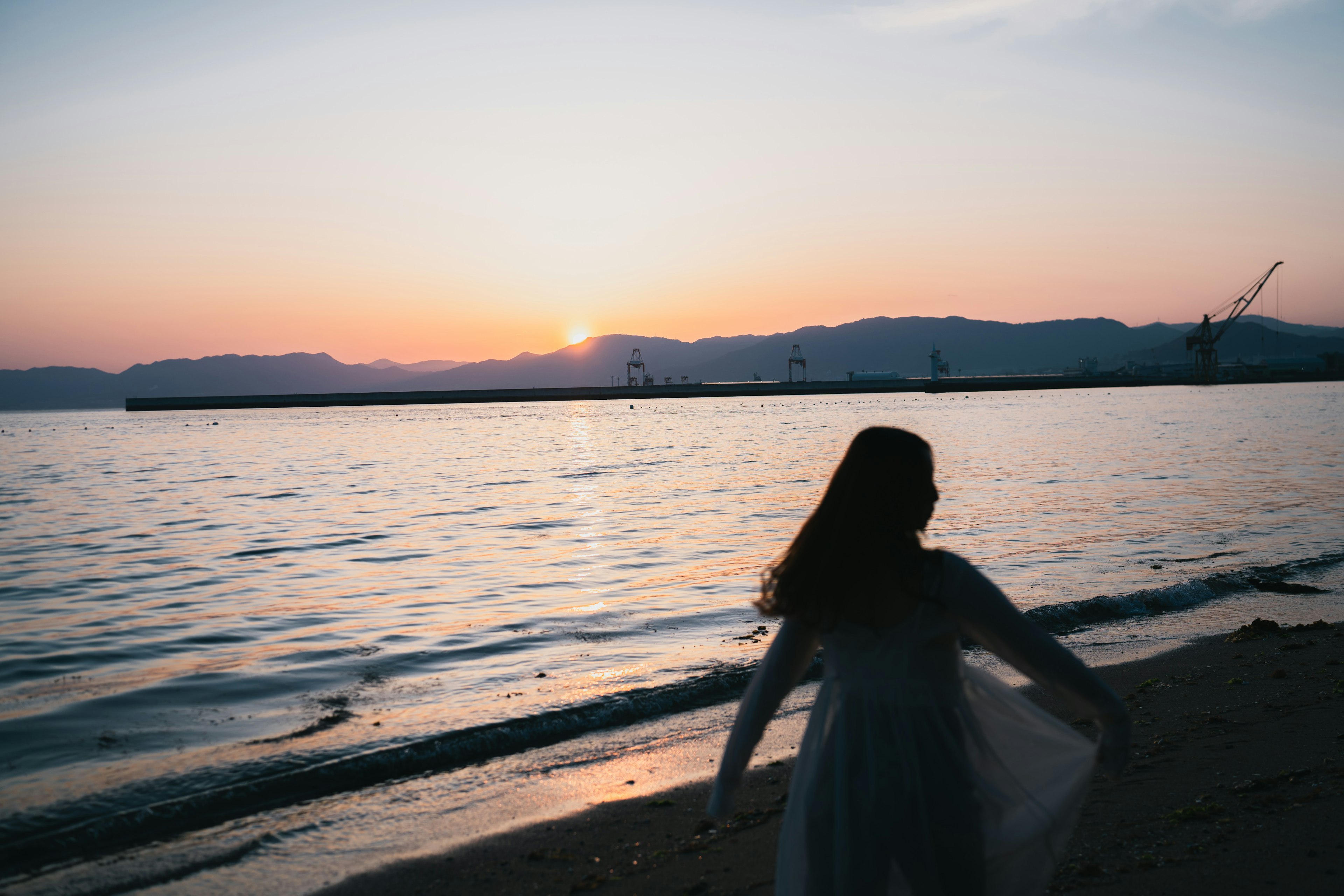 海辺で夕日を背にしている女性のシルエット