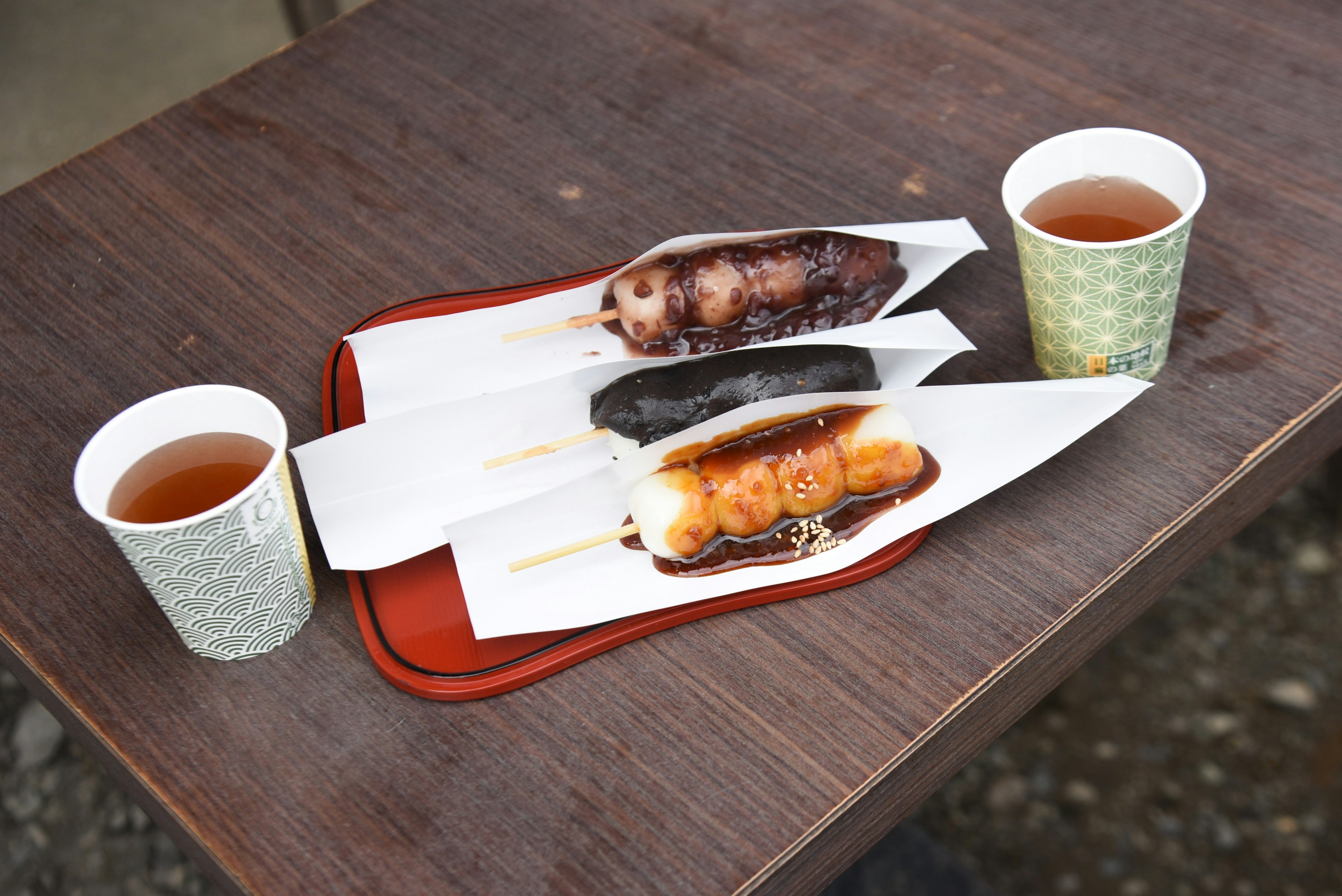 Three skewered sweet rice dumplings on a plate with cups of green tea