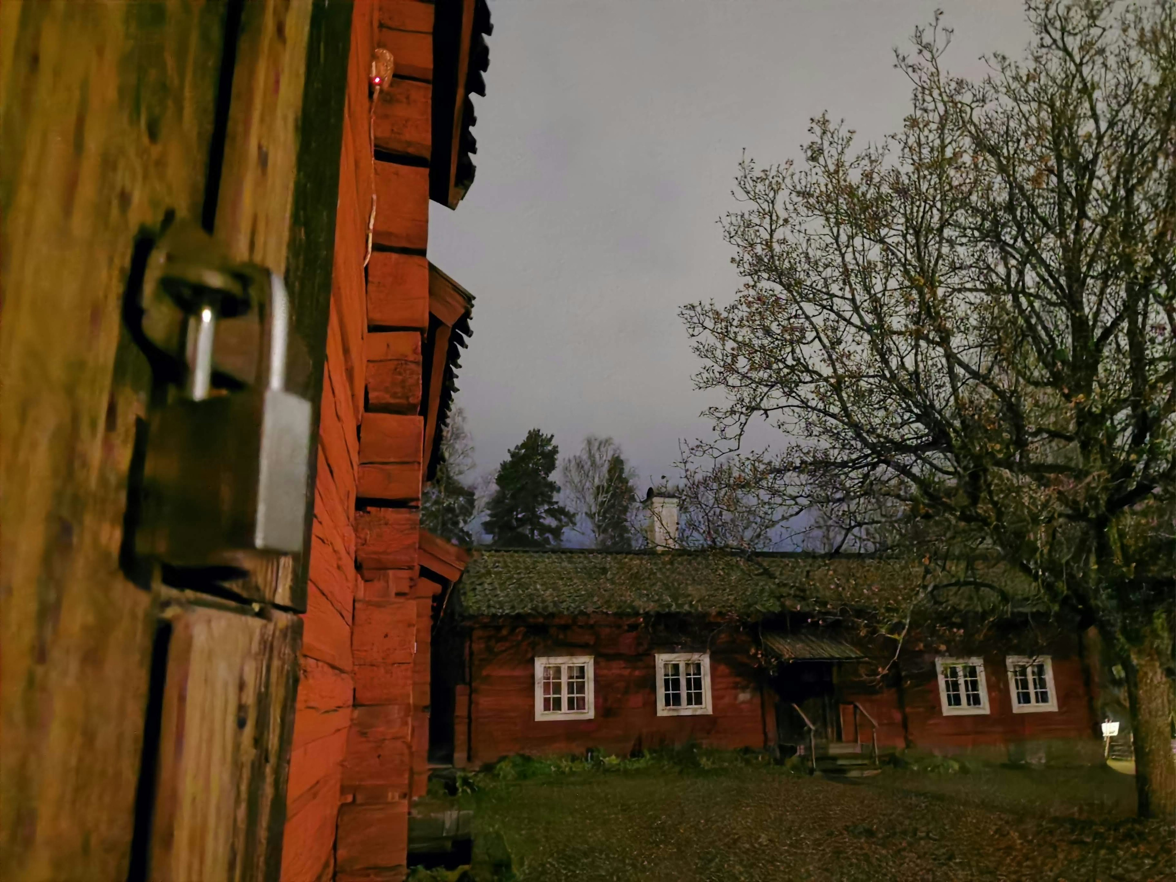 Scena buia con un edificio in legno rosso e una porta chiusa a chiave