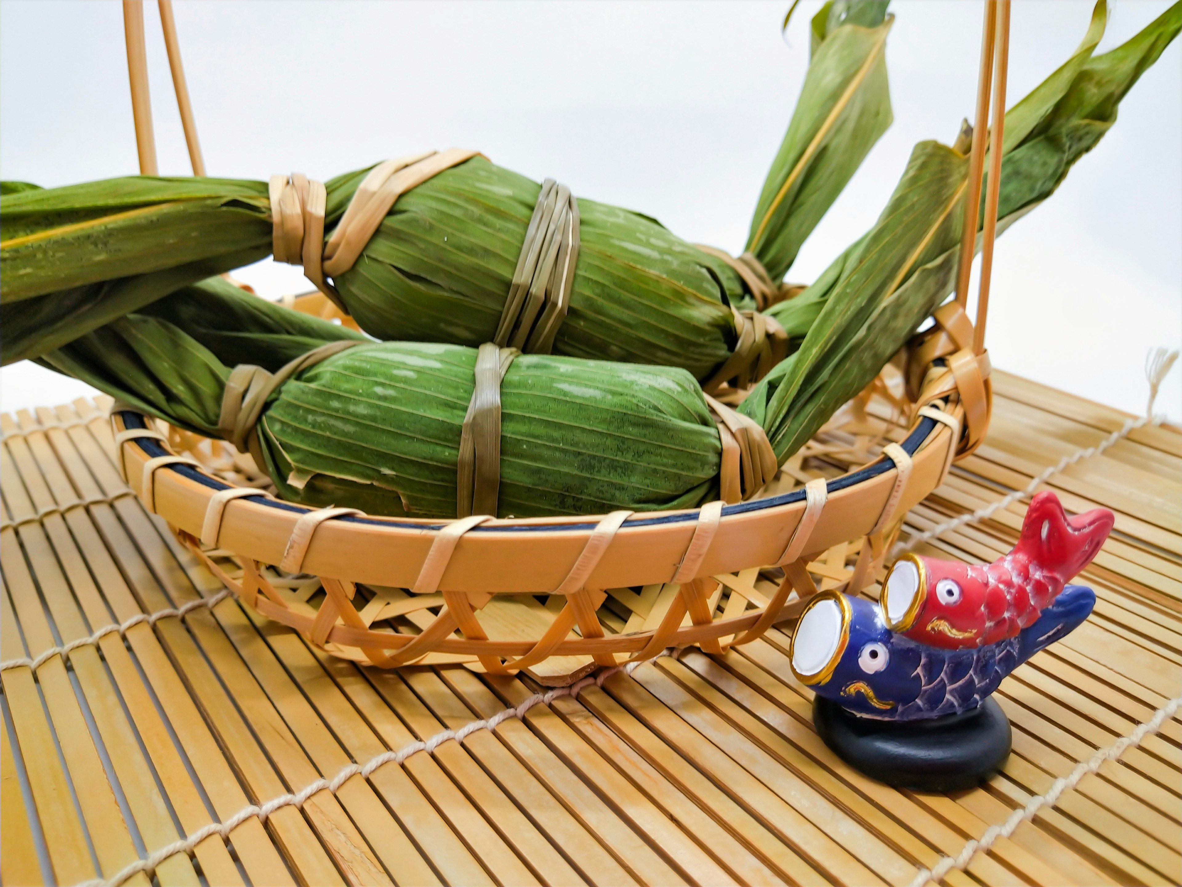 Keranjang bambu berisi makanan dibungkus daun hijau dan patung ikan kecil