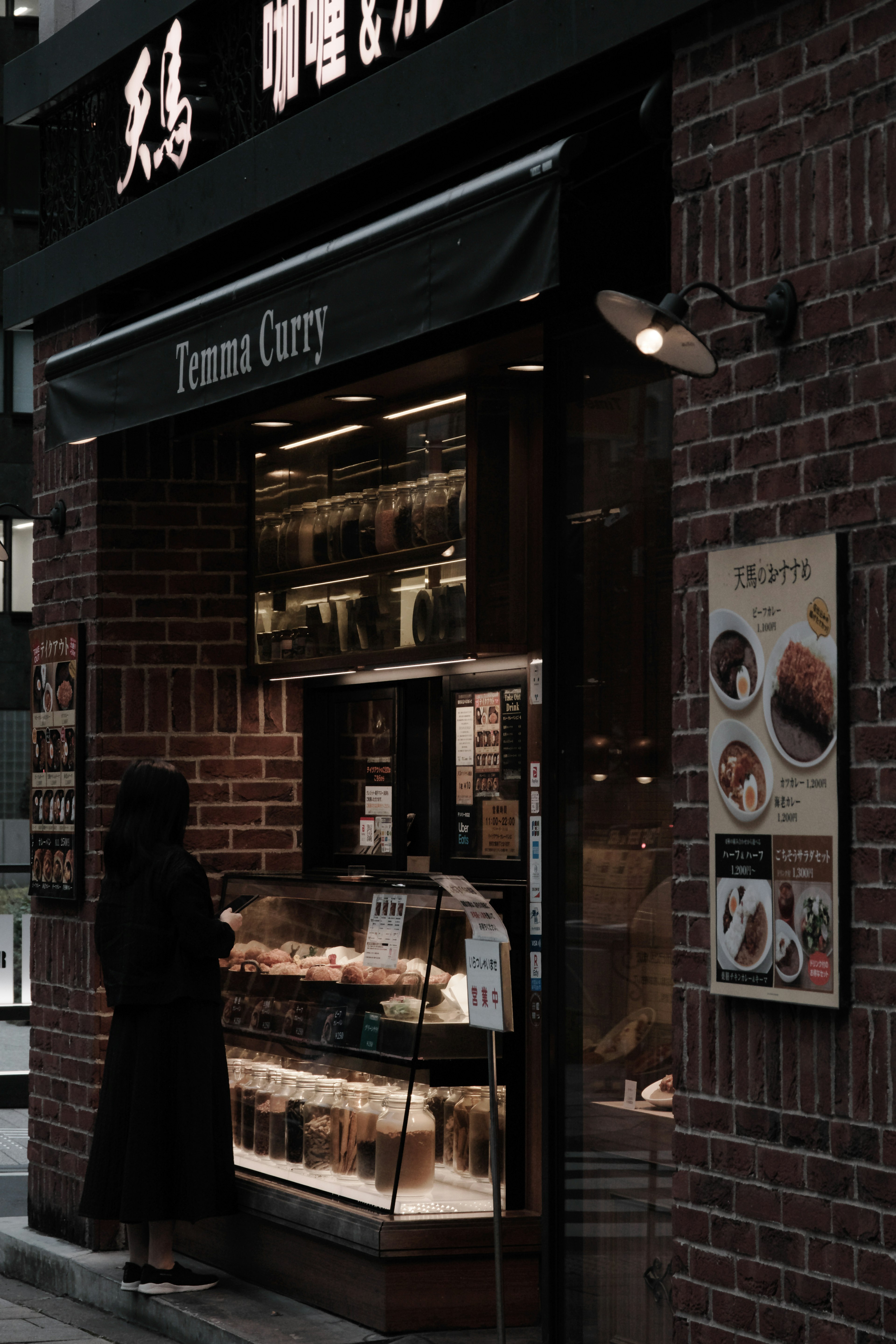 Une personne en manteau noir se tenant devant un magasin de curry tenant son extérieur