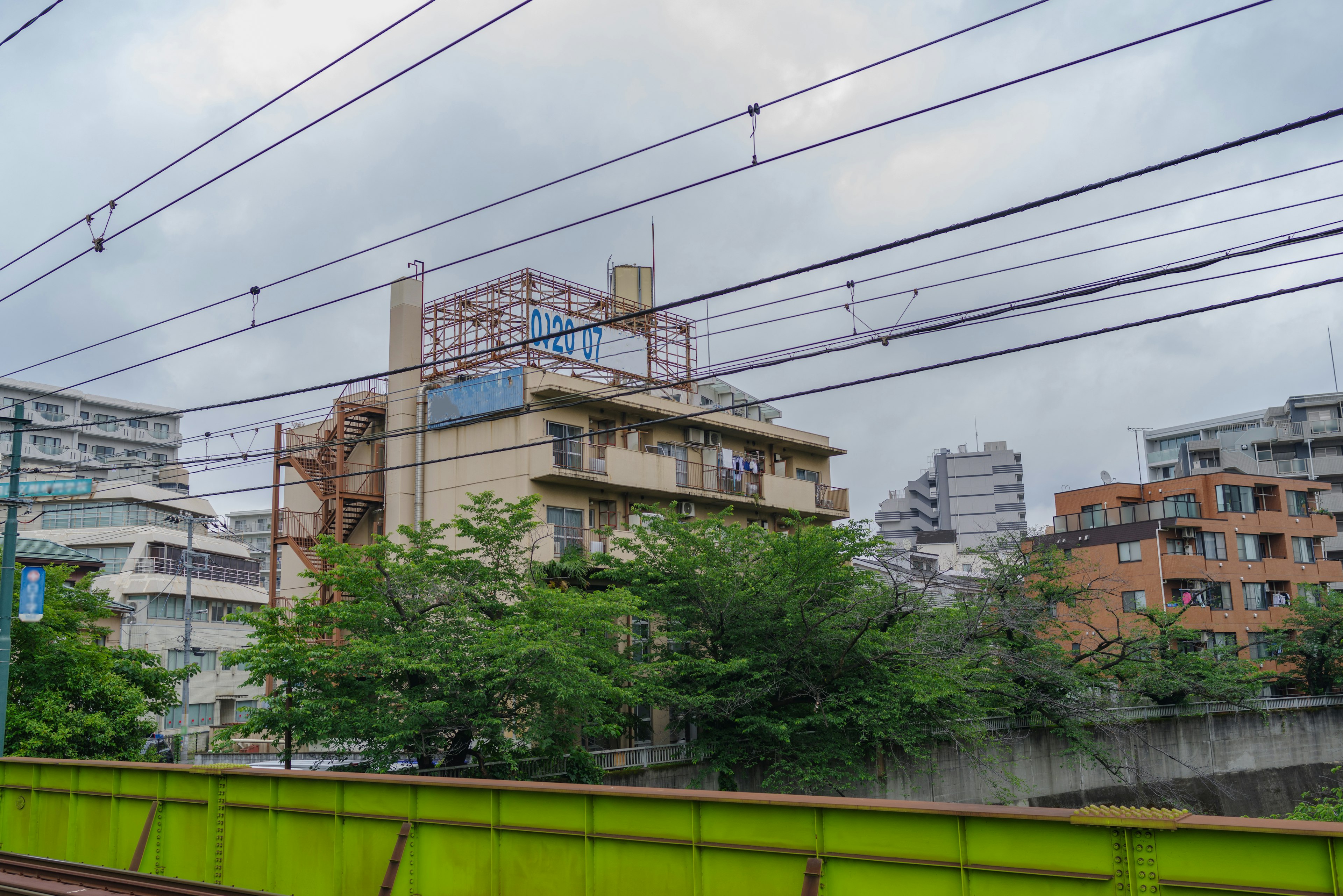 View of a building and trees near green fence and railway tracks