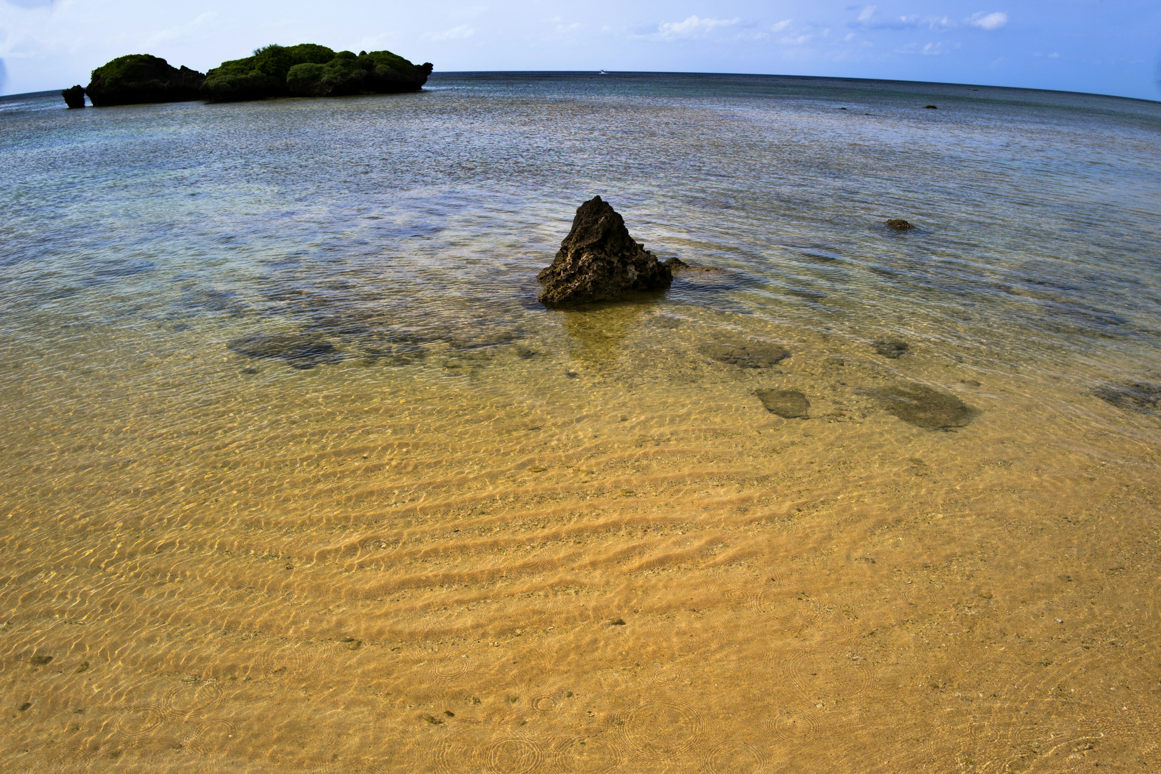 Malersiche Aussicht auf den blauen Ozean und den Sandstrand mit einem kleinen Felsen