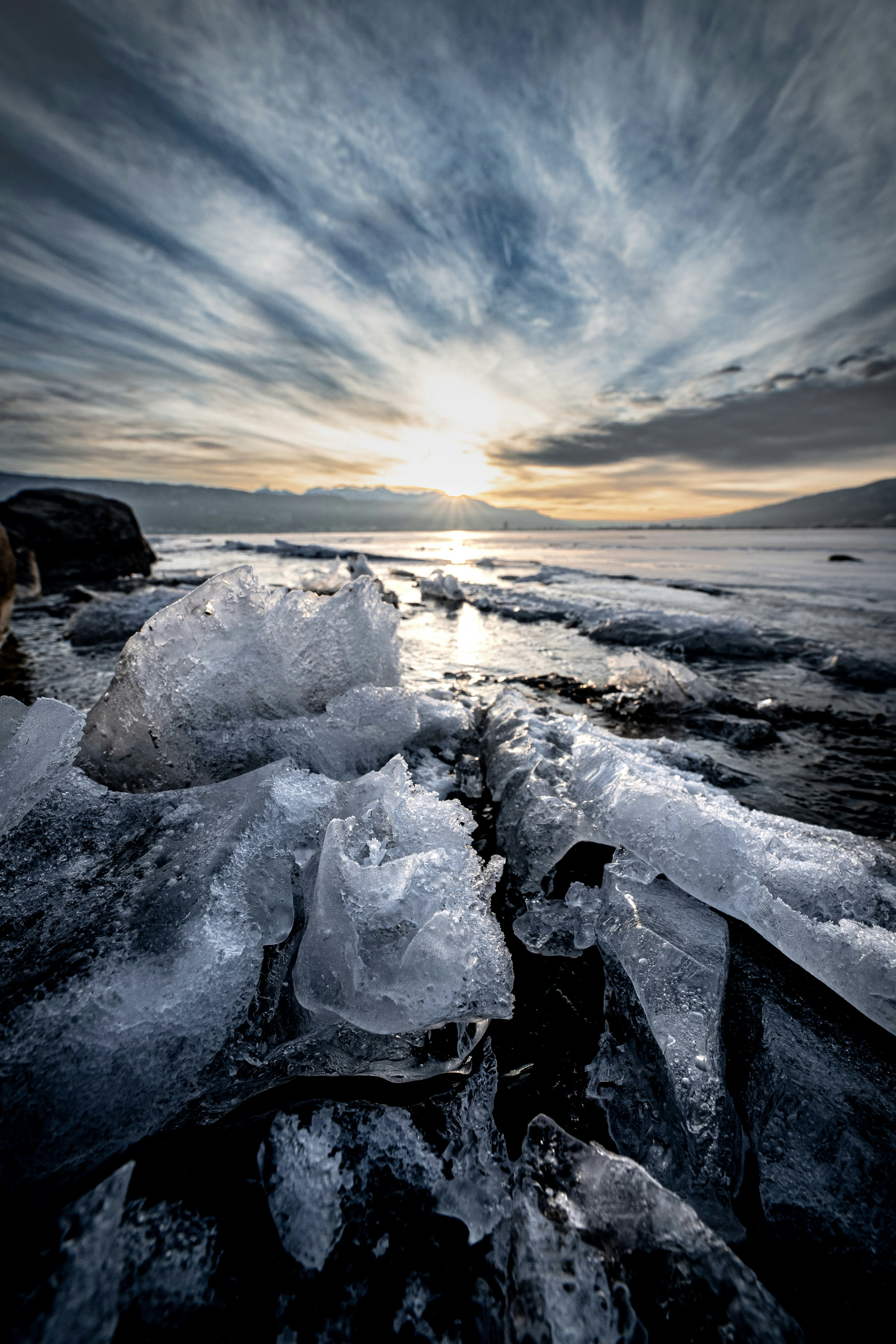 Eisformationen im Vordergrund mit einem dramatischen Sonnenuntergang über dem Meer