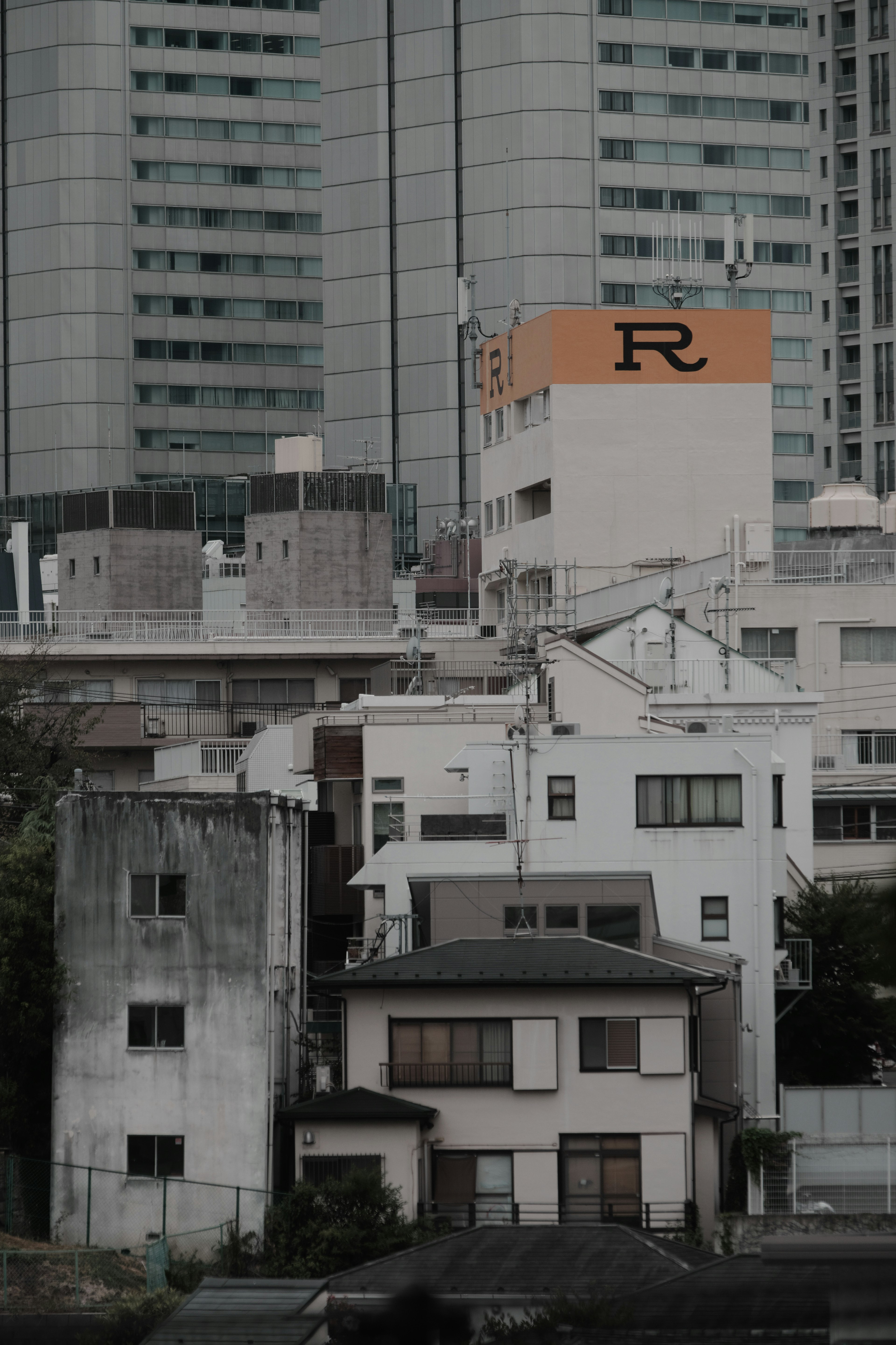 Urban landscape featuring a mix of high-rise buildings and older houses with a prominent orange 'R' logo