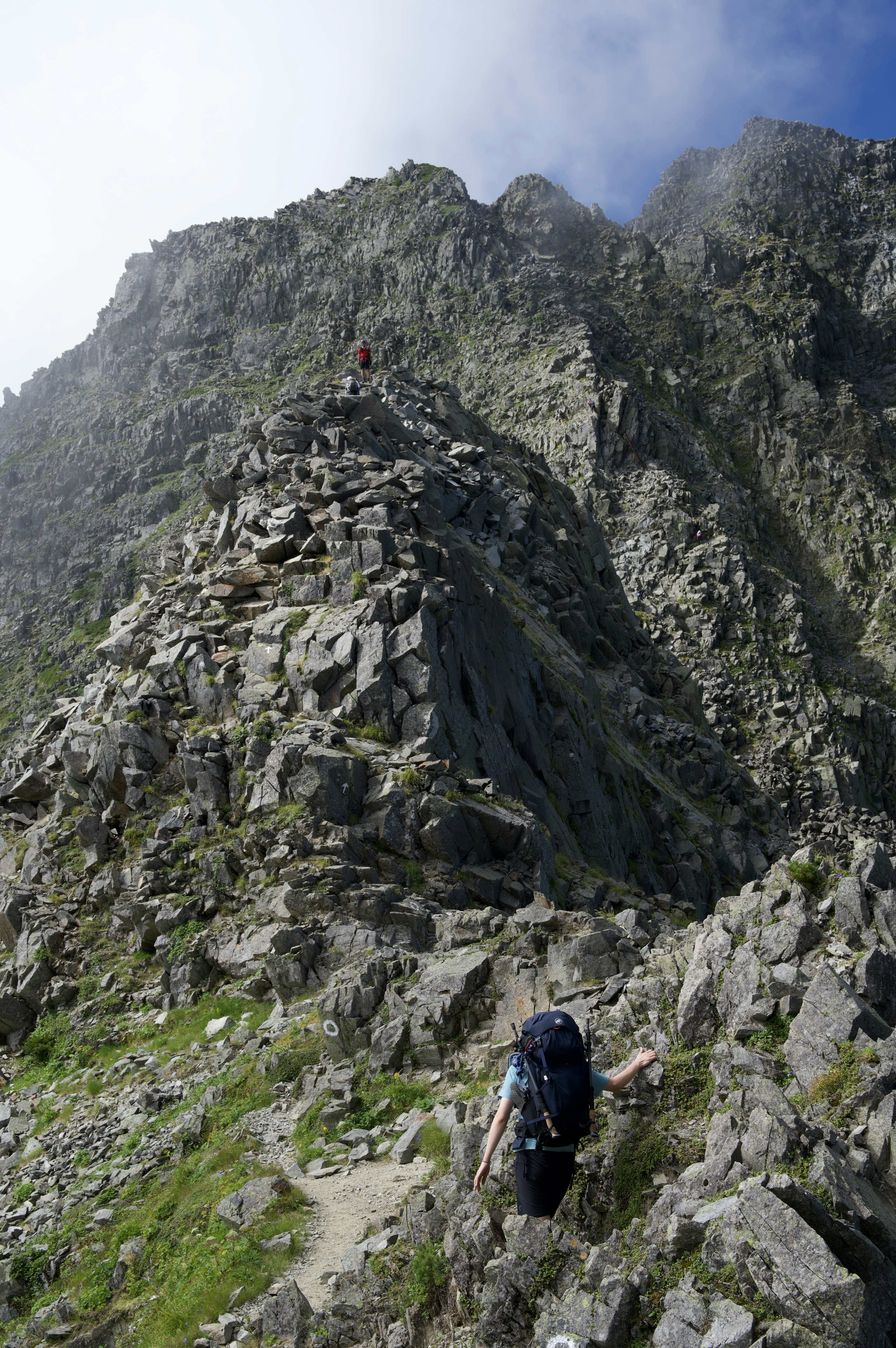 Senderista subiendo un sendero montañoso rocoso con acantilados empinados