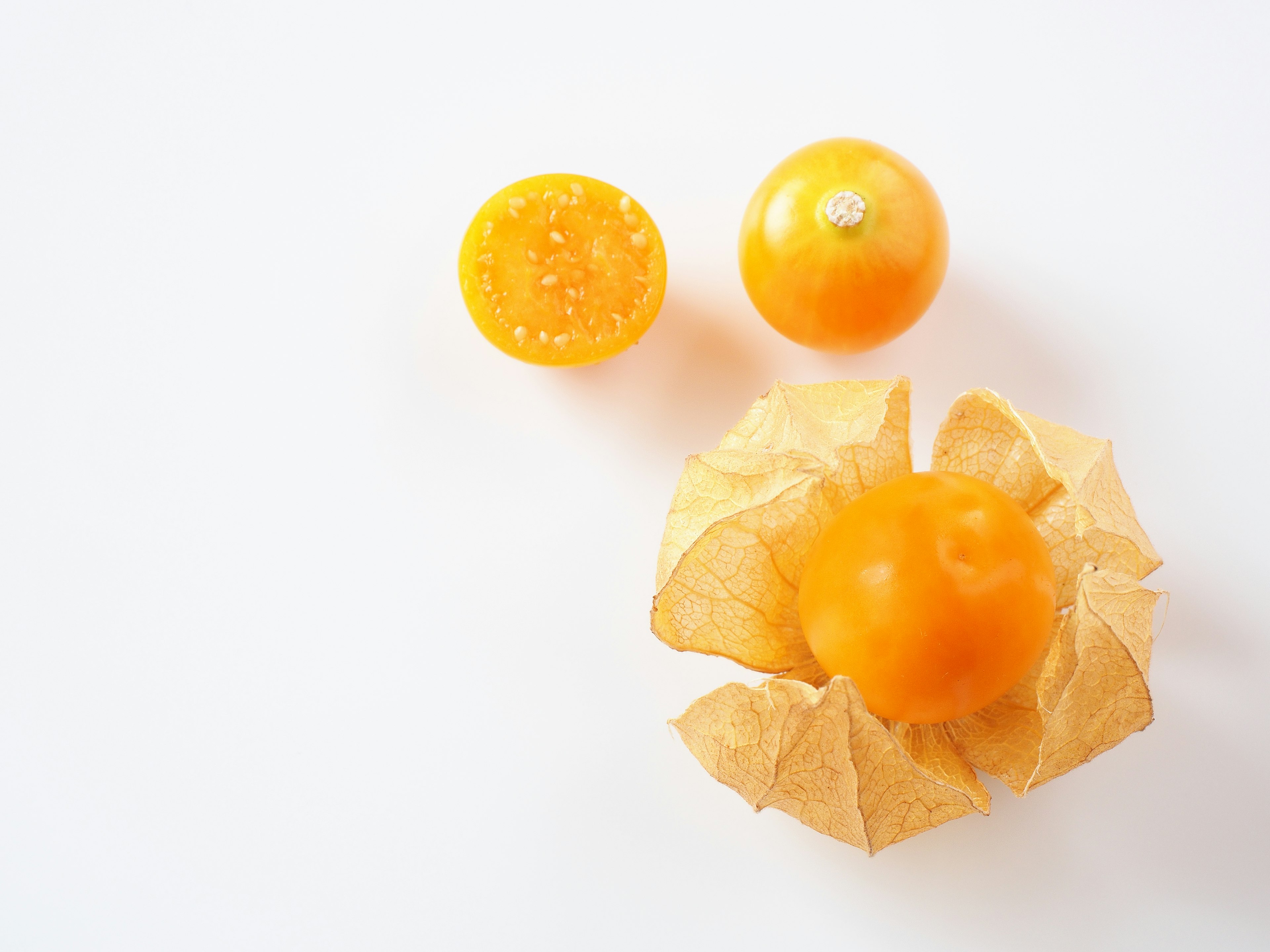 Fruta naranja con cáscara pelada y mitad cortada sobre fondo blanco