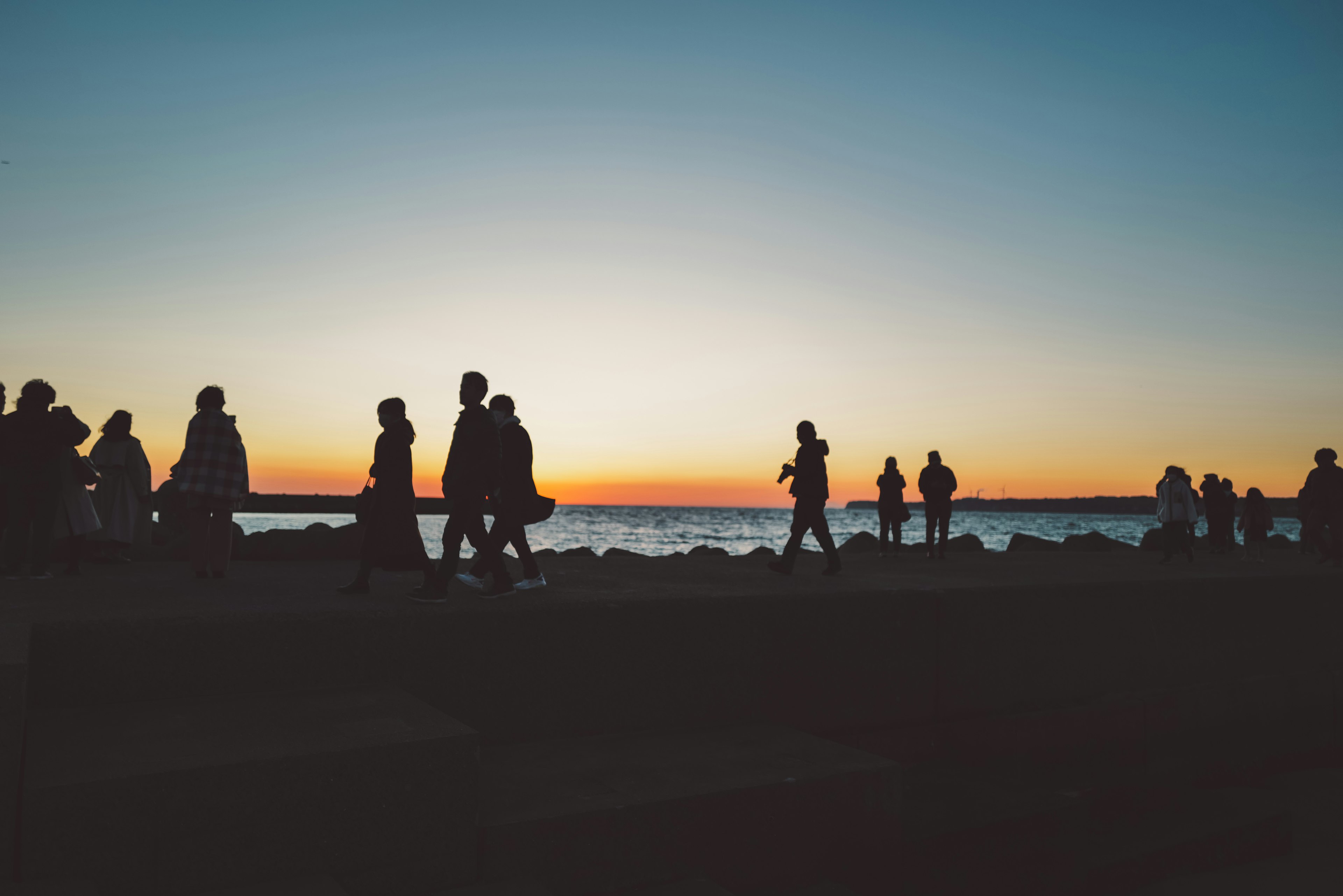 夕暮れ時の海岸を歩く人々のシルエット