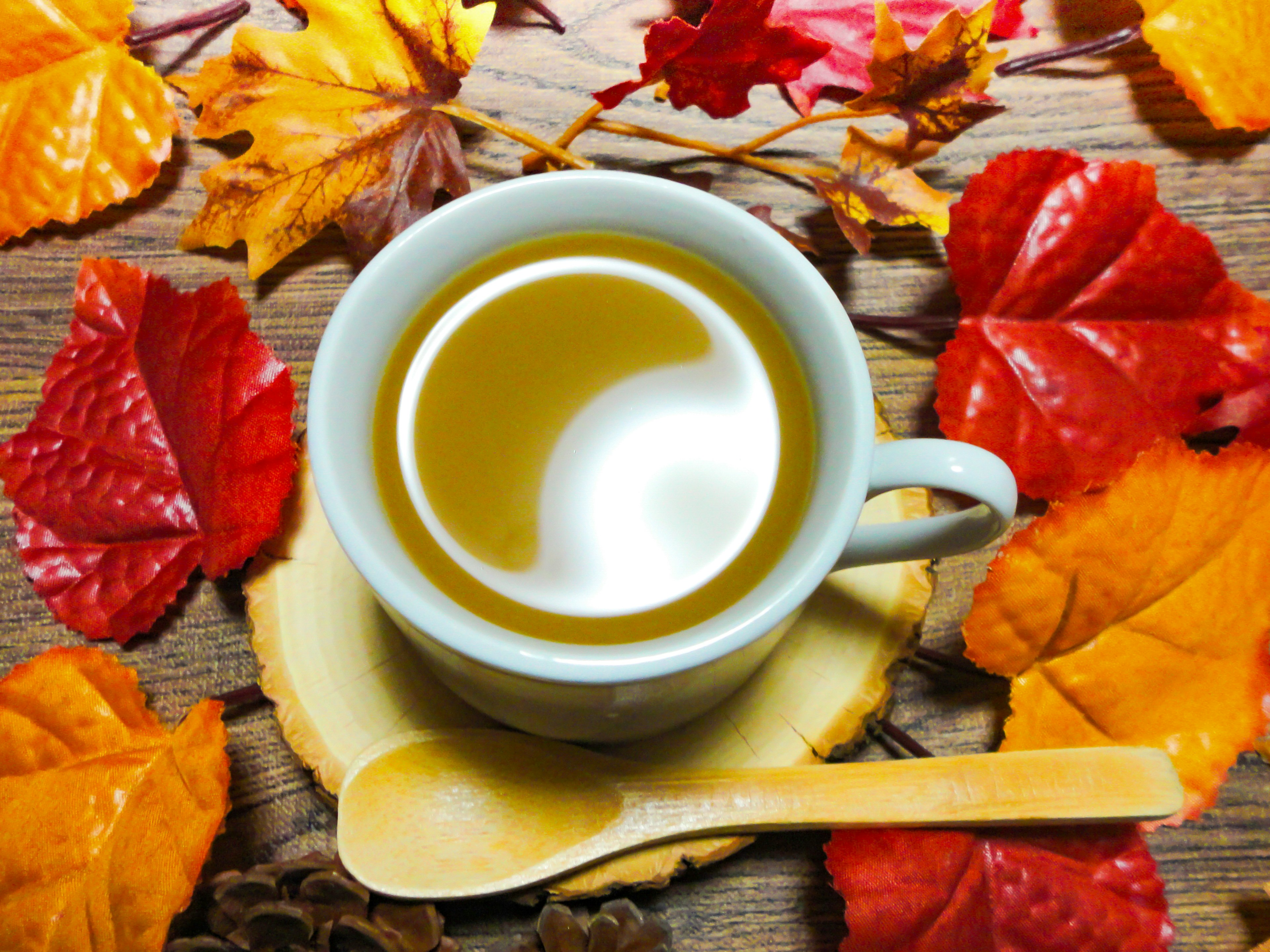 Warm beverage in a cup surrounded by autumn leaves