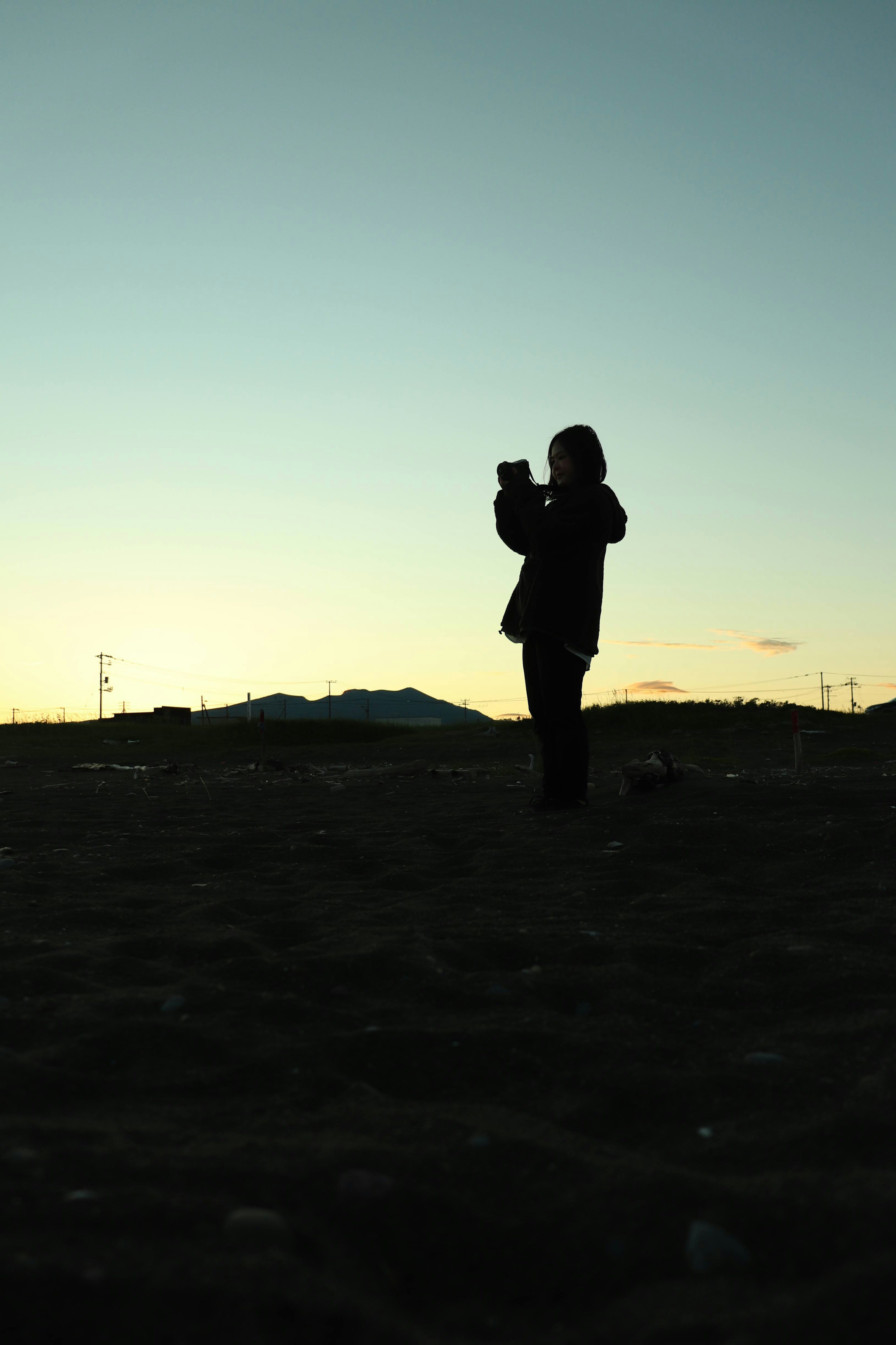 Silhouette di una persona che tiene una macchina fotografica contro un tramonto