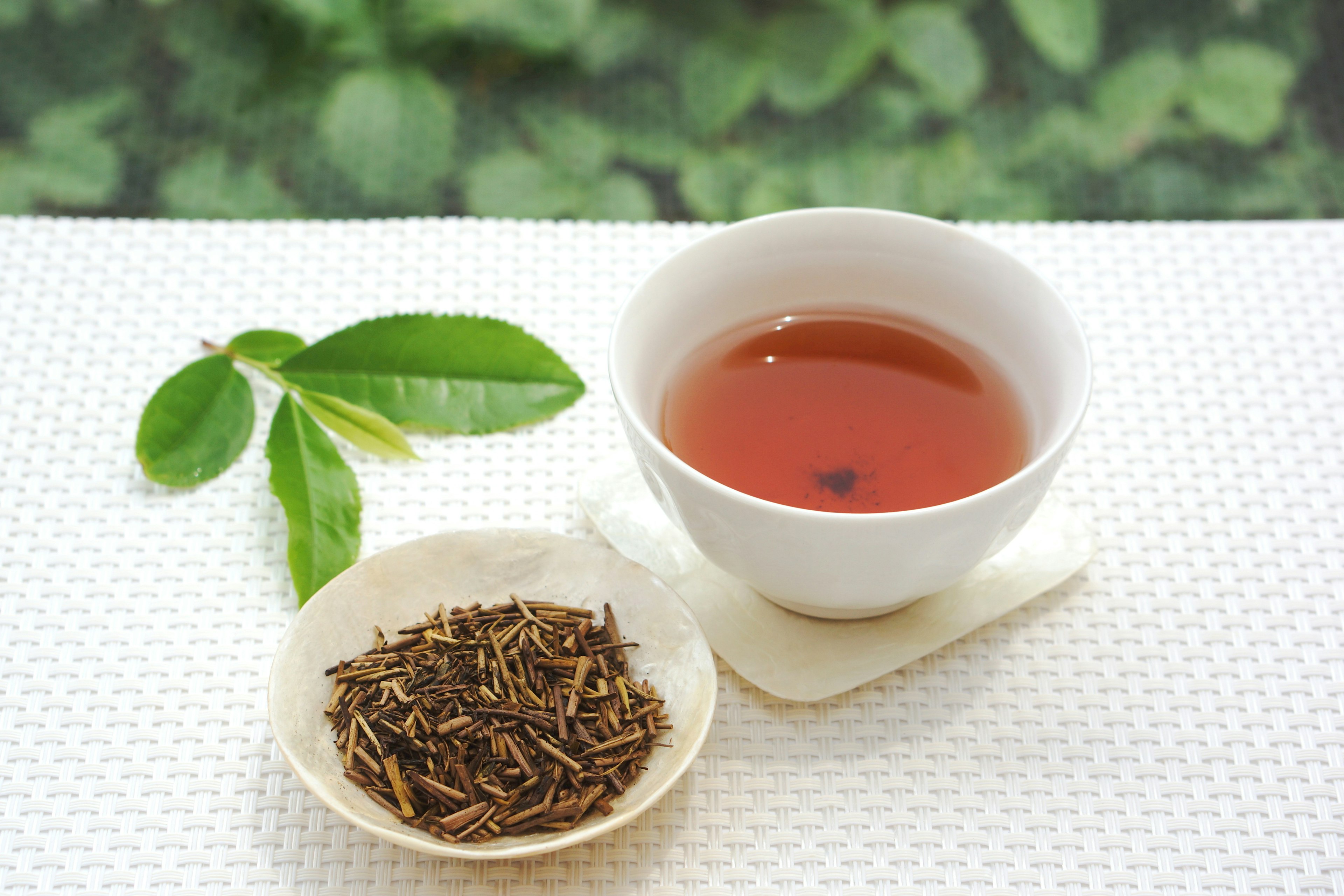 A cup of tea with loose tea leaves and a green leaf nearby