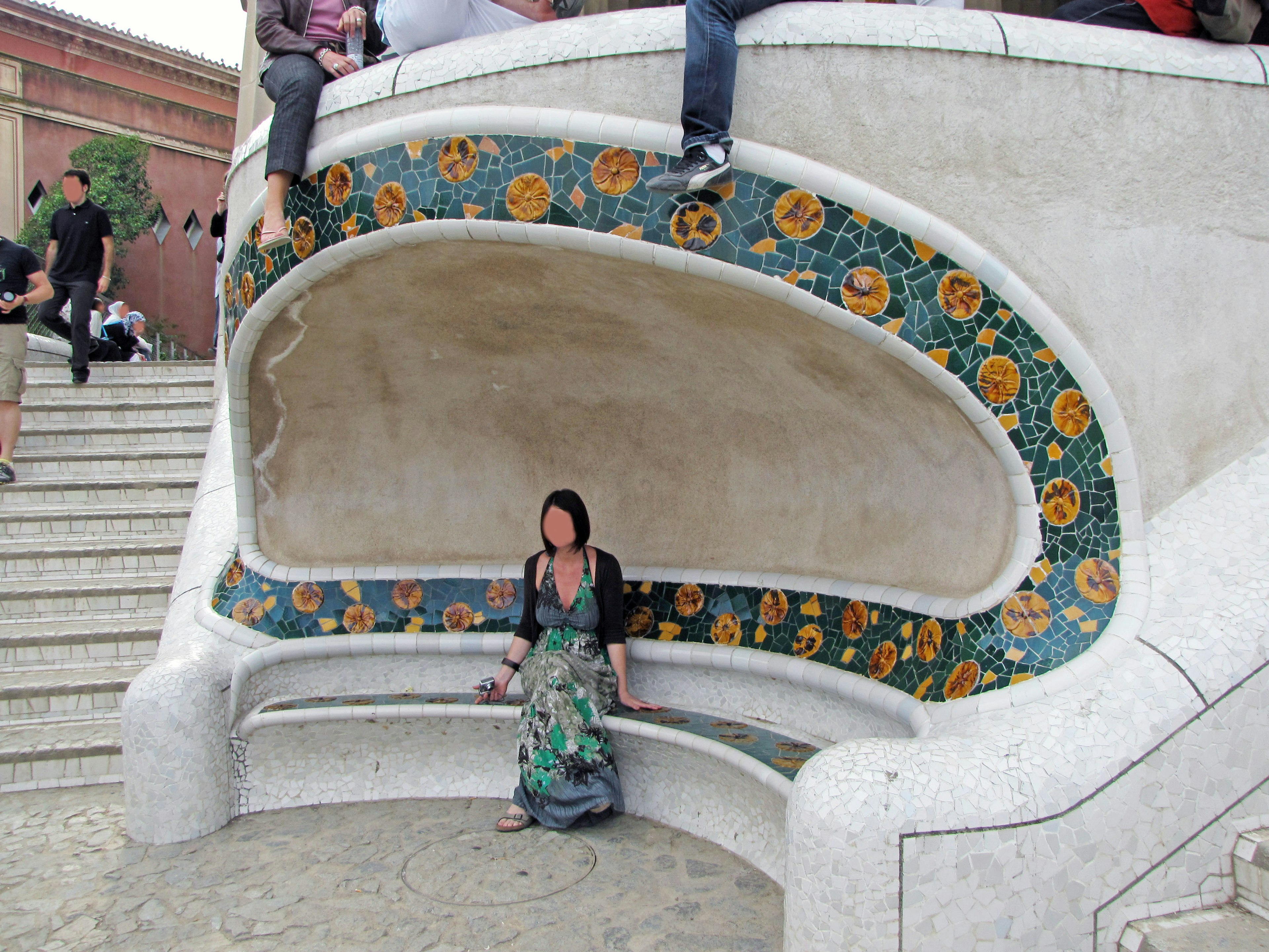 Eine Frau sitzt auf einer bunten gefliesten Bank im Park Güell