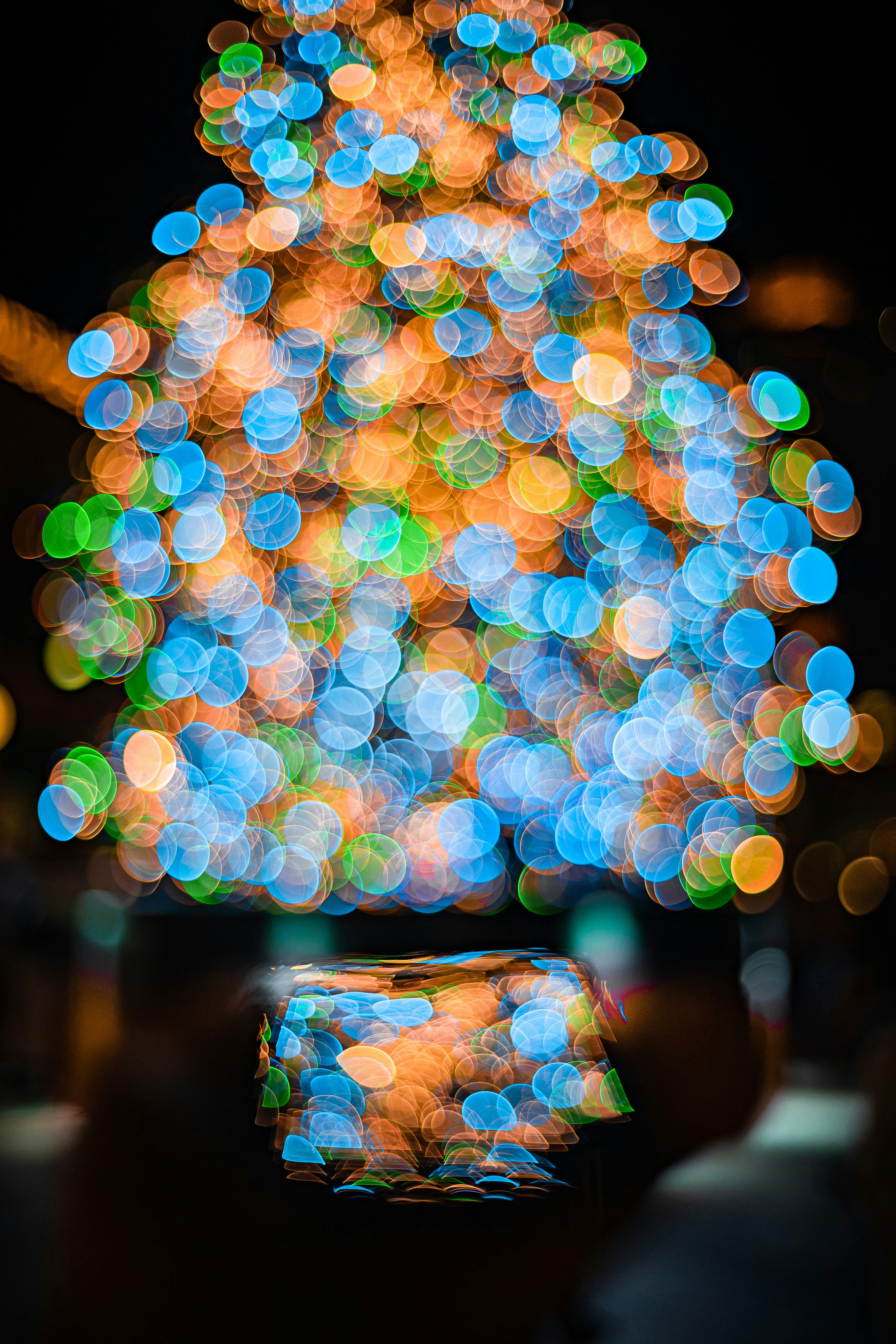 Una mano che tiene uno smartphone davanti a un albero di Natale sfocato con luci colorate