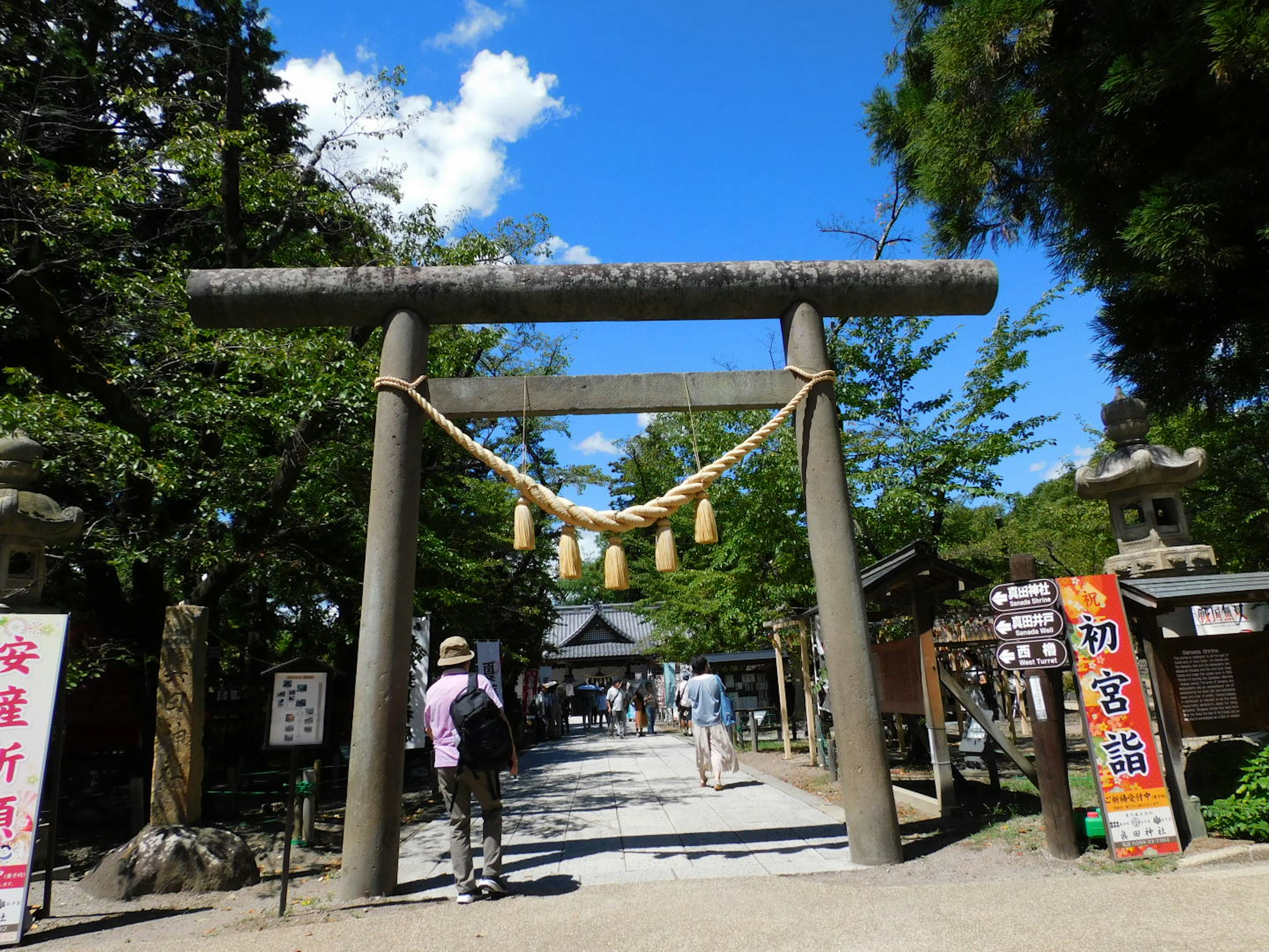 Cổng torii dưới bầu trời xanh với con đường dẫn đến đền thờ du khách đang đi bộ