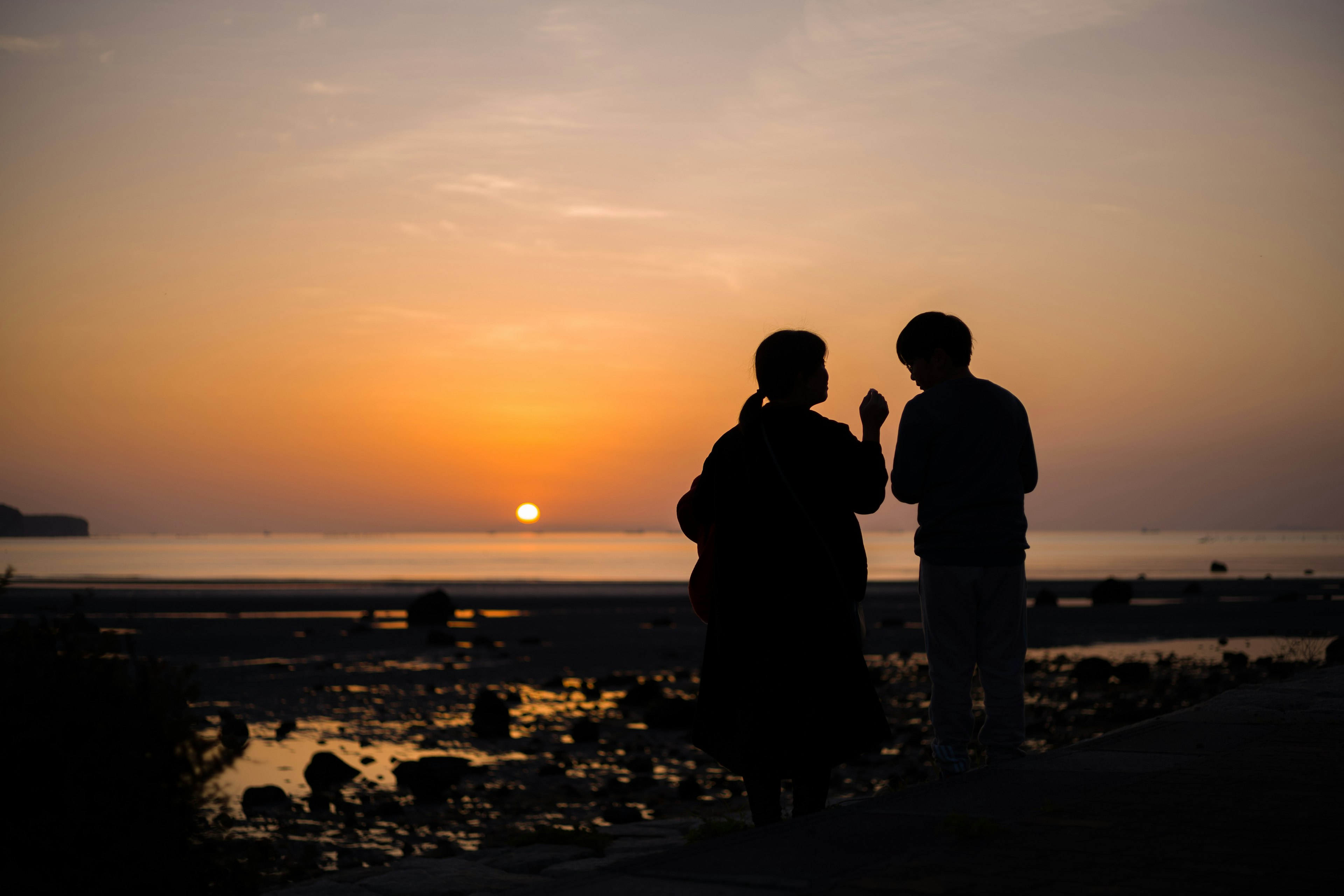 Silhouette of two people talking against a sunset over the sea