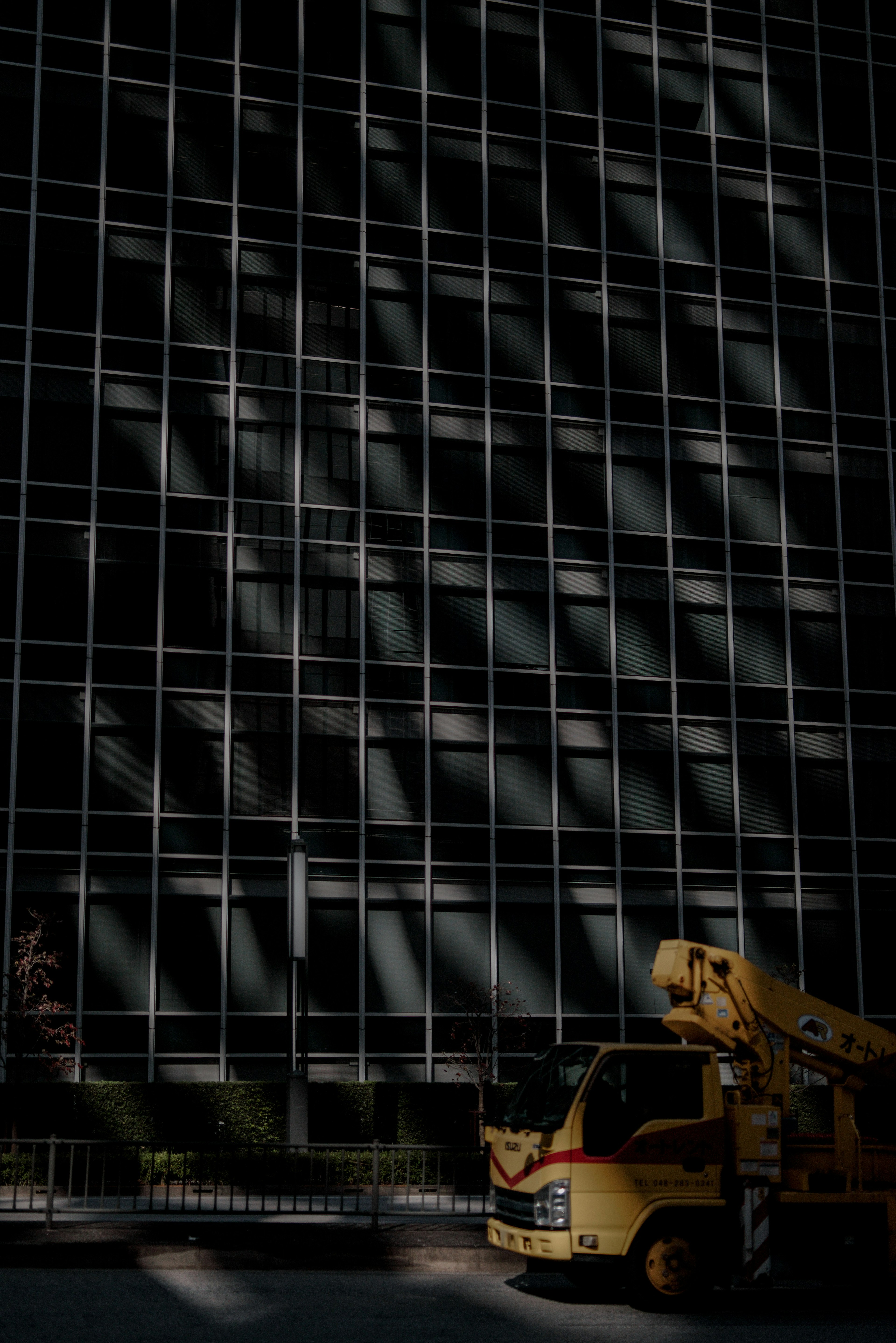 Contrast of a building's glass facade and a yellow crane truck