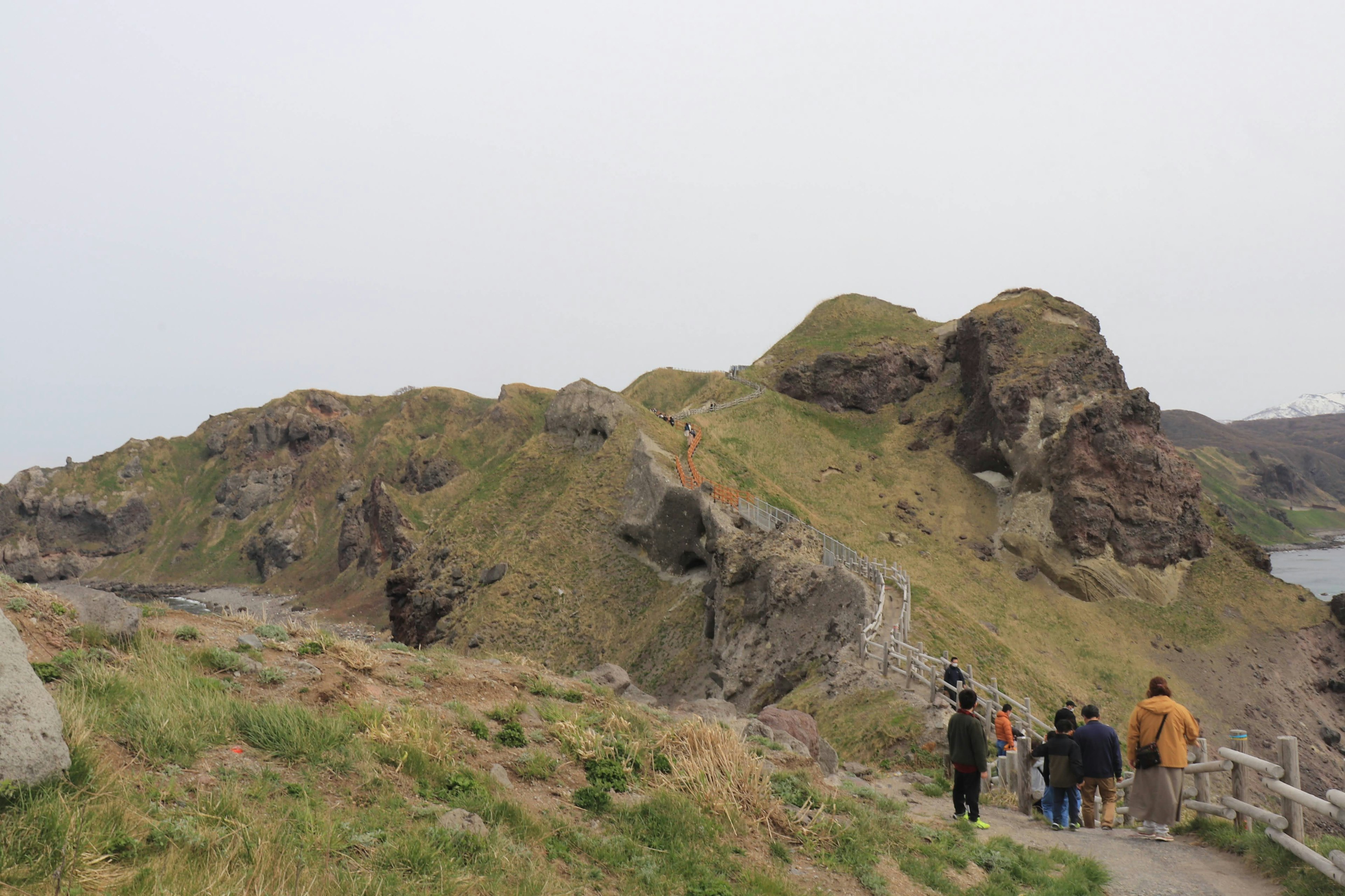 People walking along a coastal path with green grass and rocky hills