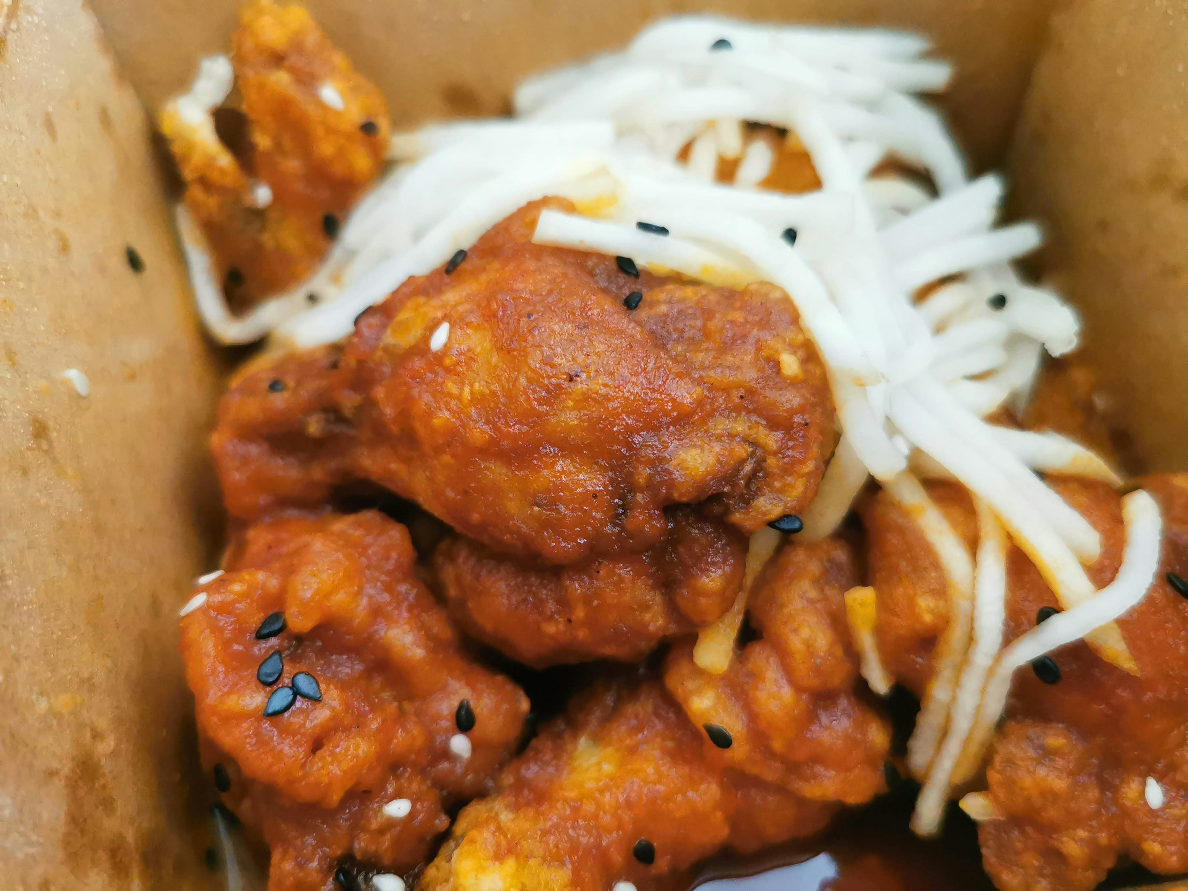 Spicy chicken pieces with white vegetables in a takeout box