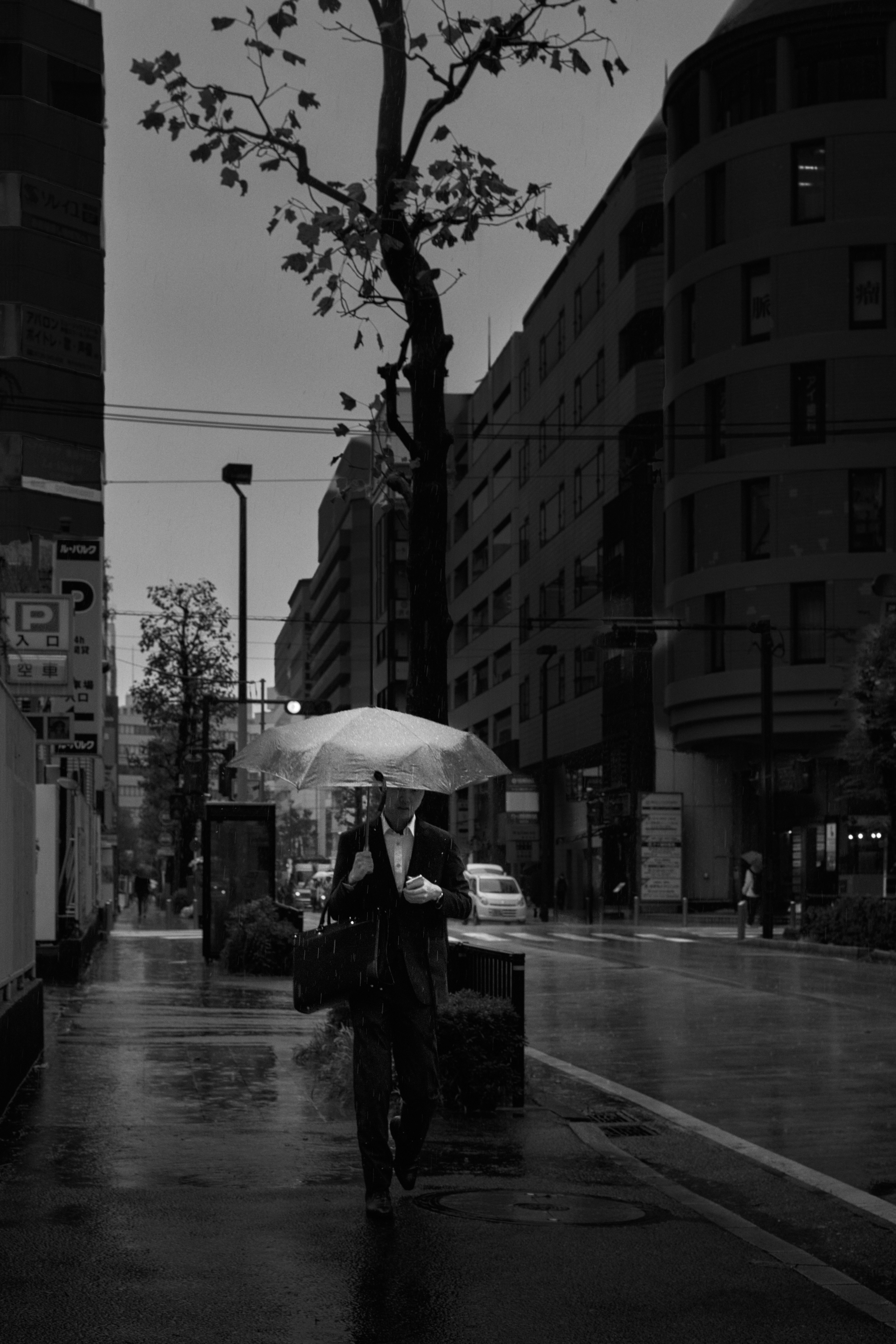 Schwarzweißfoto einer Person, die mit einem Regenschirm im Regen geht Stadtlandschaft im Hintergrund