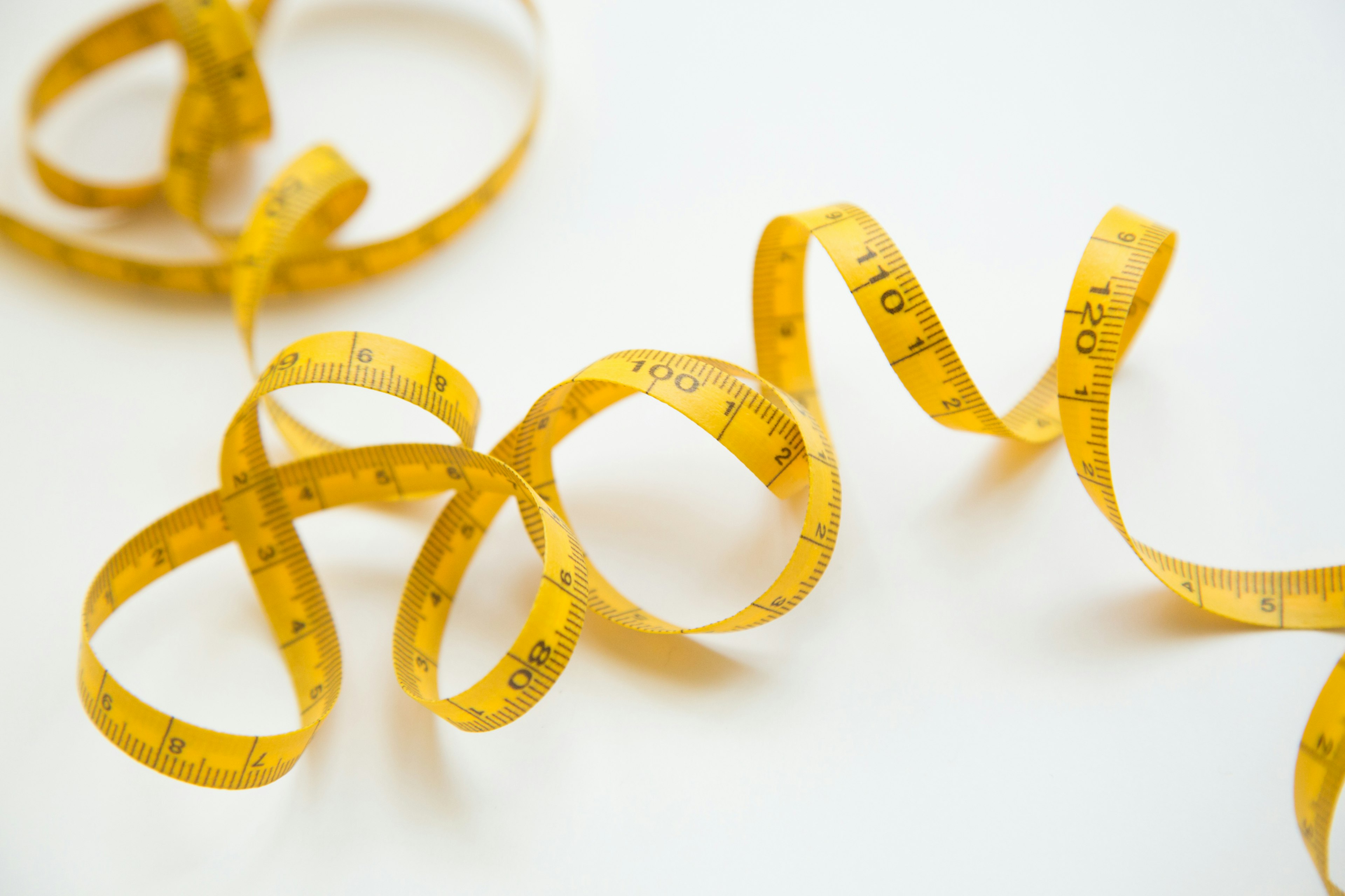 Yellow measuring tape coiled on a white background