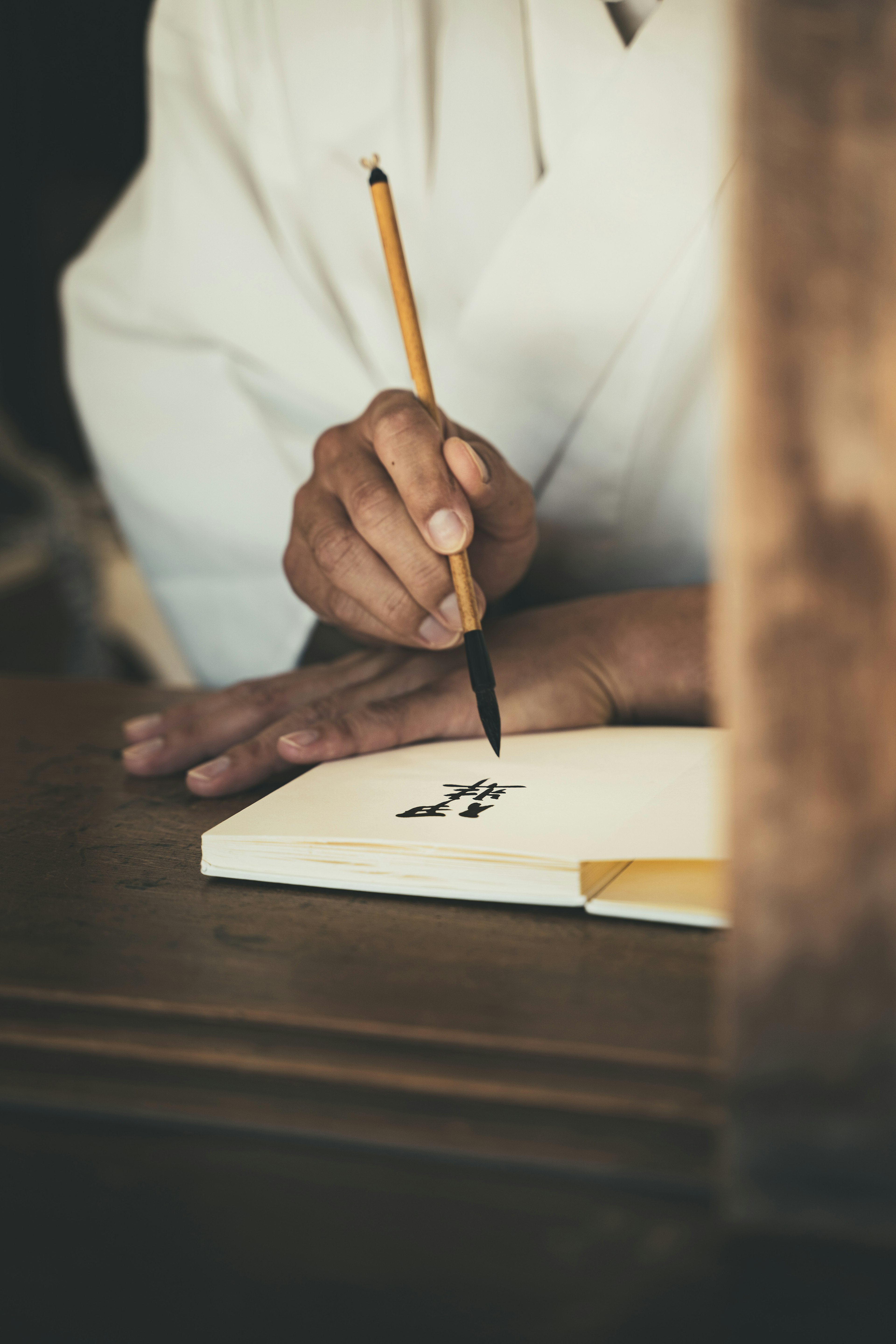 A hand holding a brush writing on a notebook with a white garment