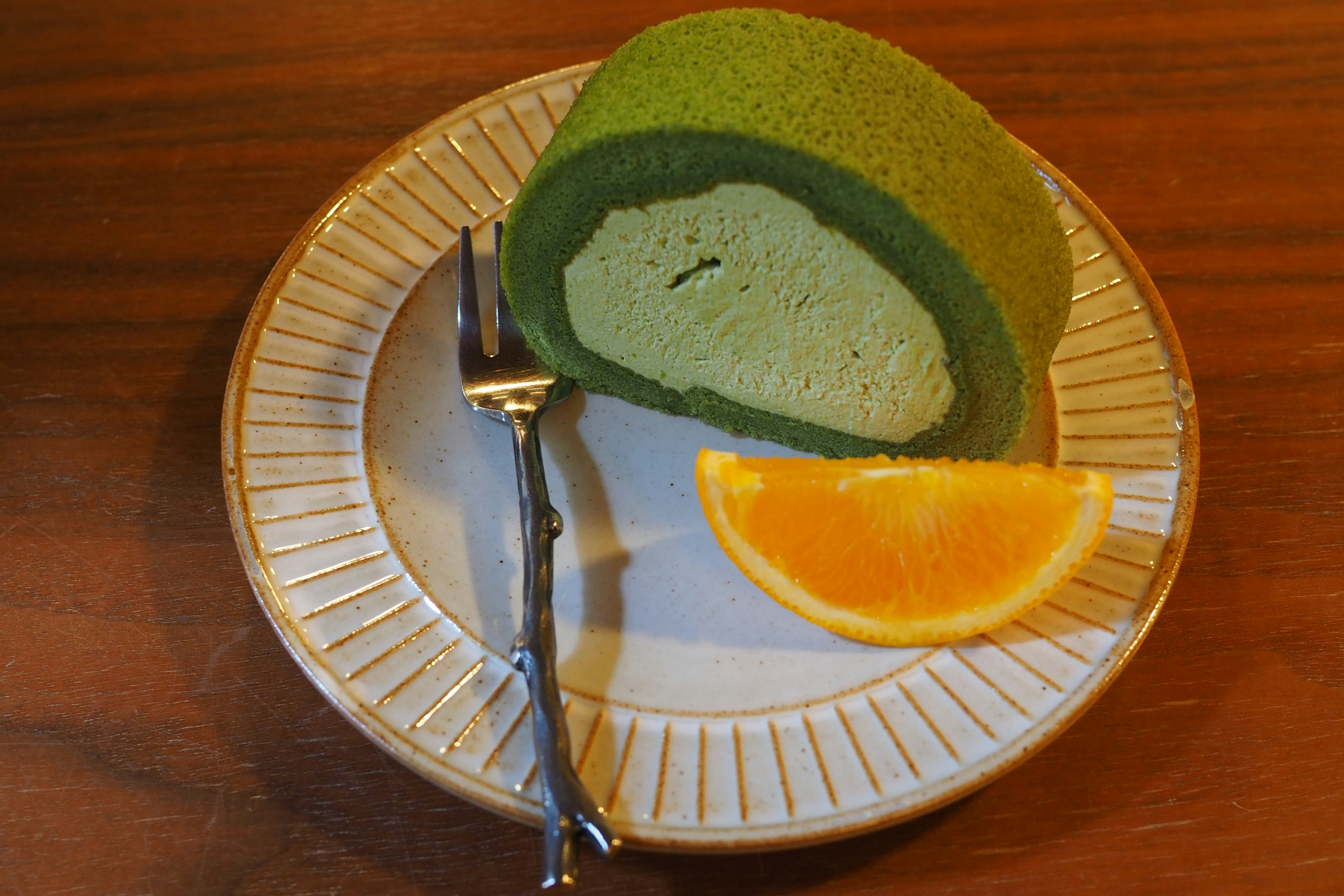 Un pastel enrollado verde con una rodaja de naranja en un plato