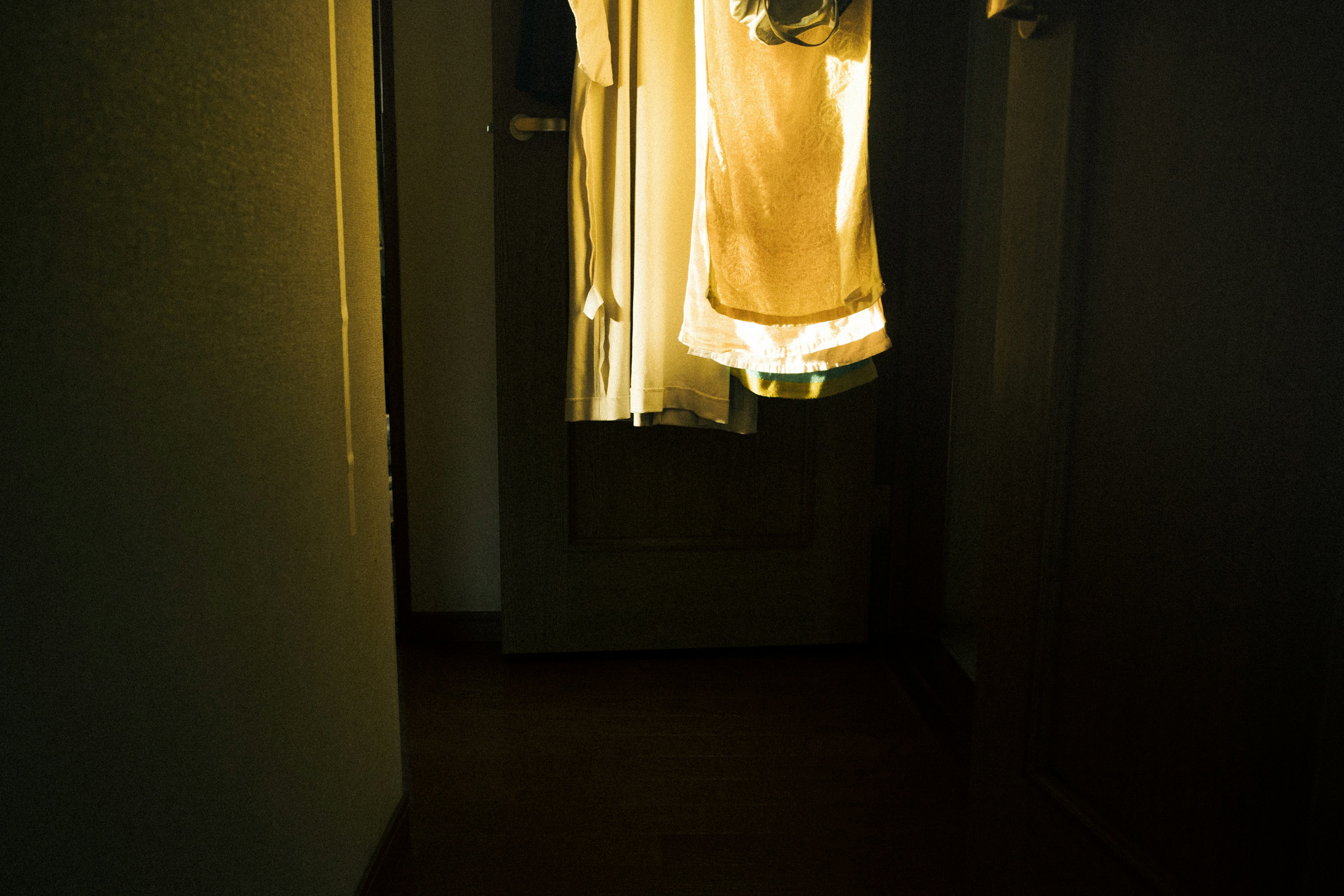 Dimly lit hallway with clothes hanging and light from the door