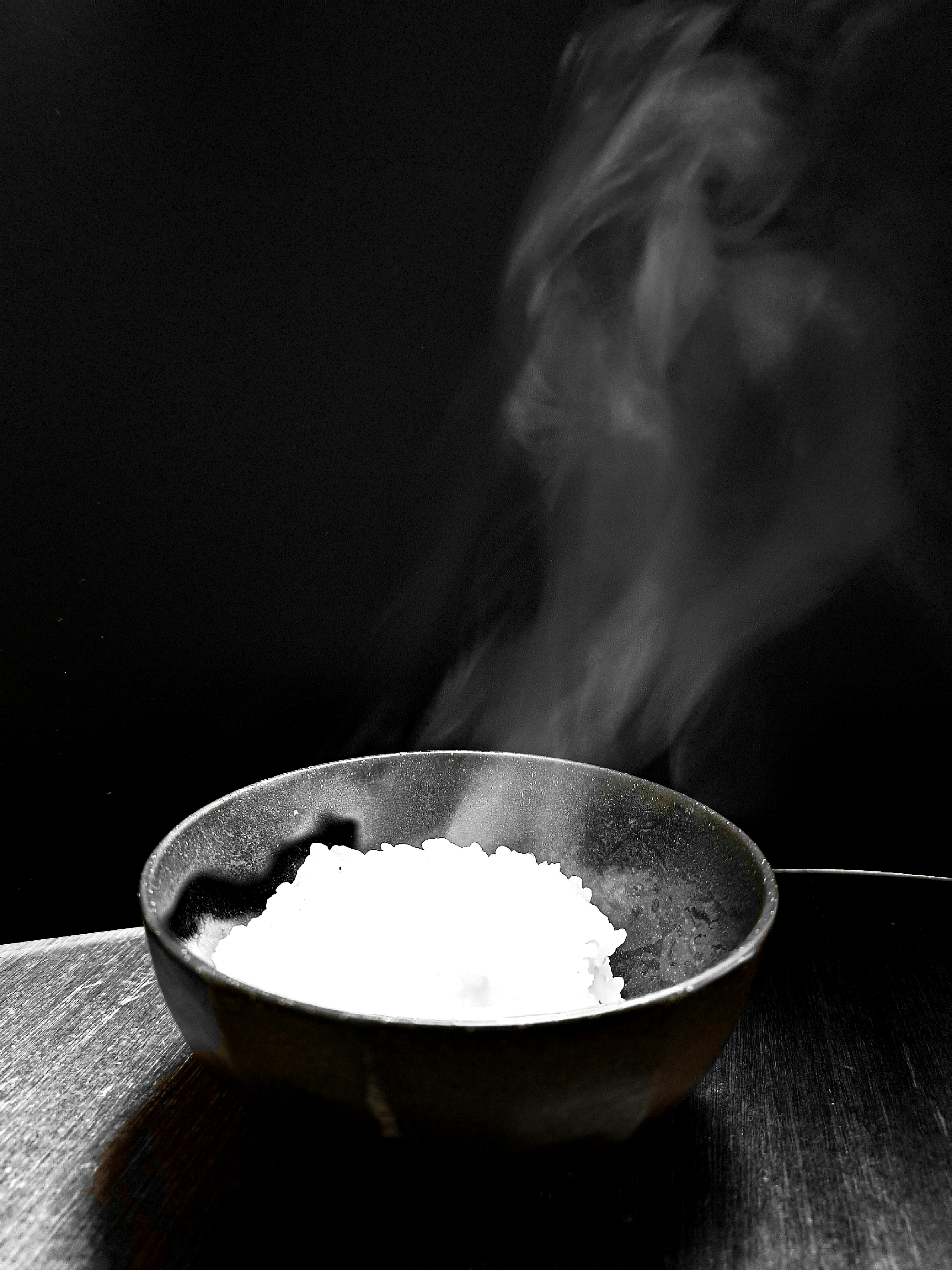 A bowl of steaming white rice against a black background