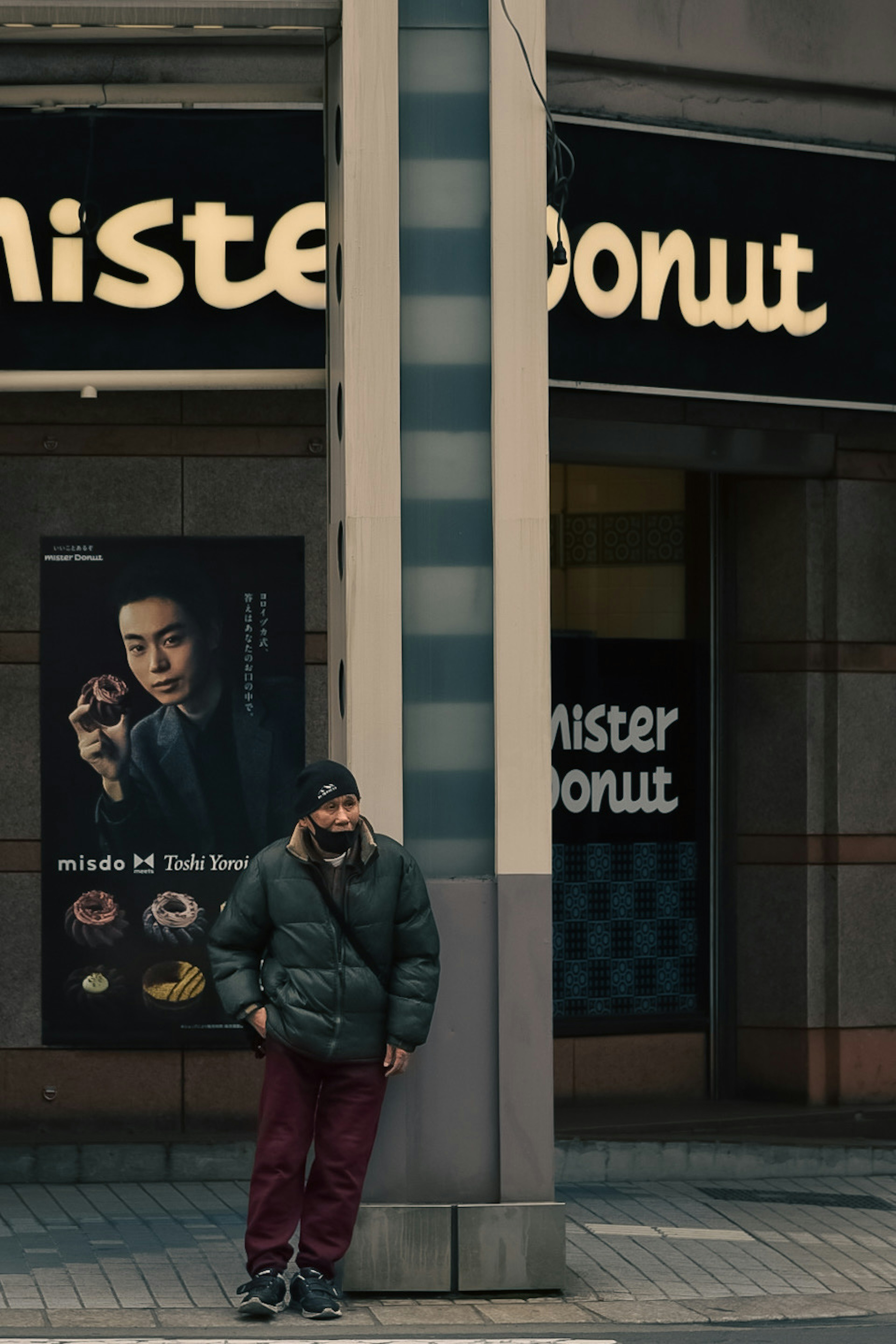 Man standing at the street corner near Mister Donut sign