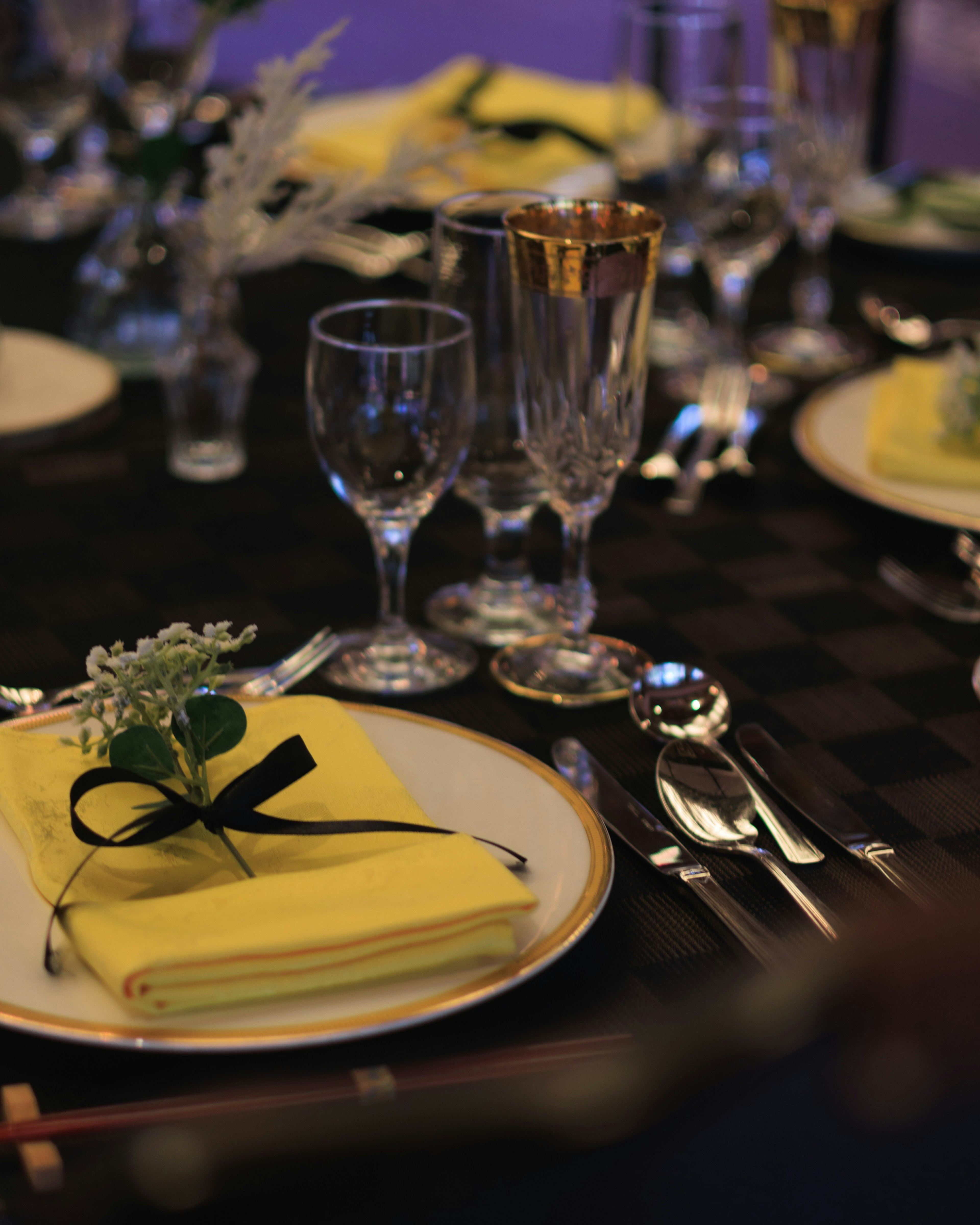 Elegant table setting featuring yellow napkin tied with black ribbon crystal glassware and decorative greenery