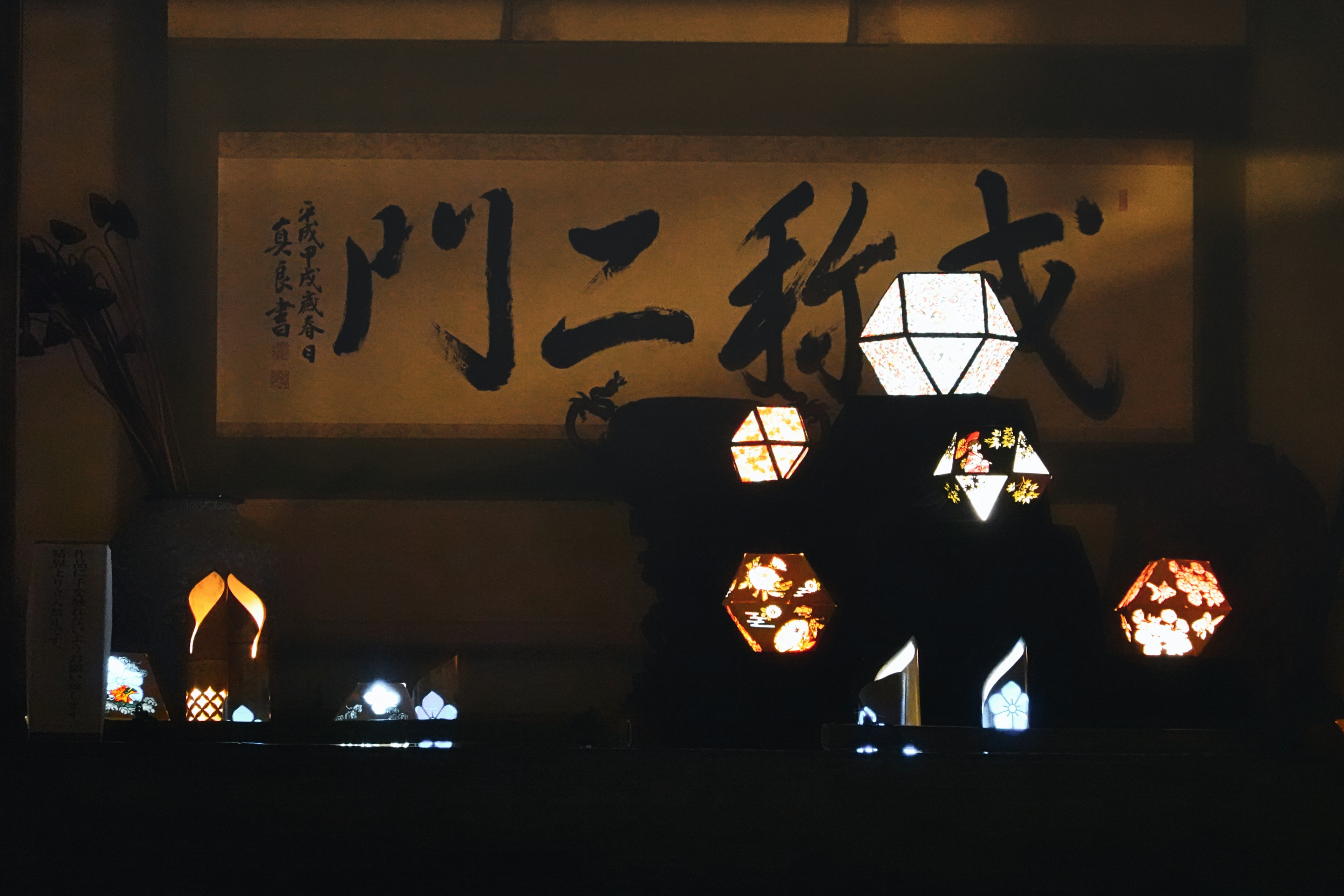 Une exposition de lampes décoratives sur fond sombre avec une grande calligraphie