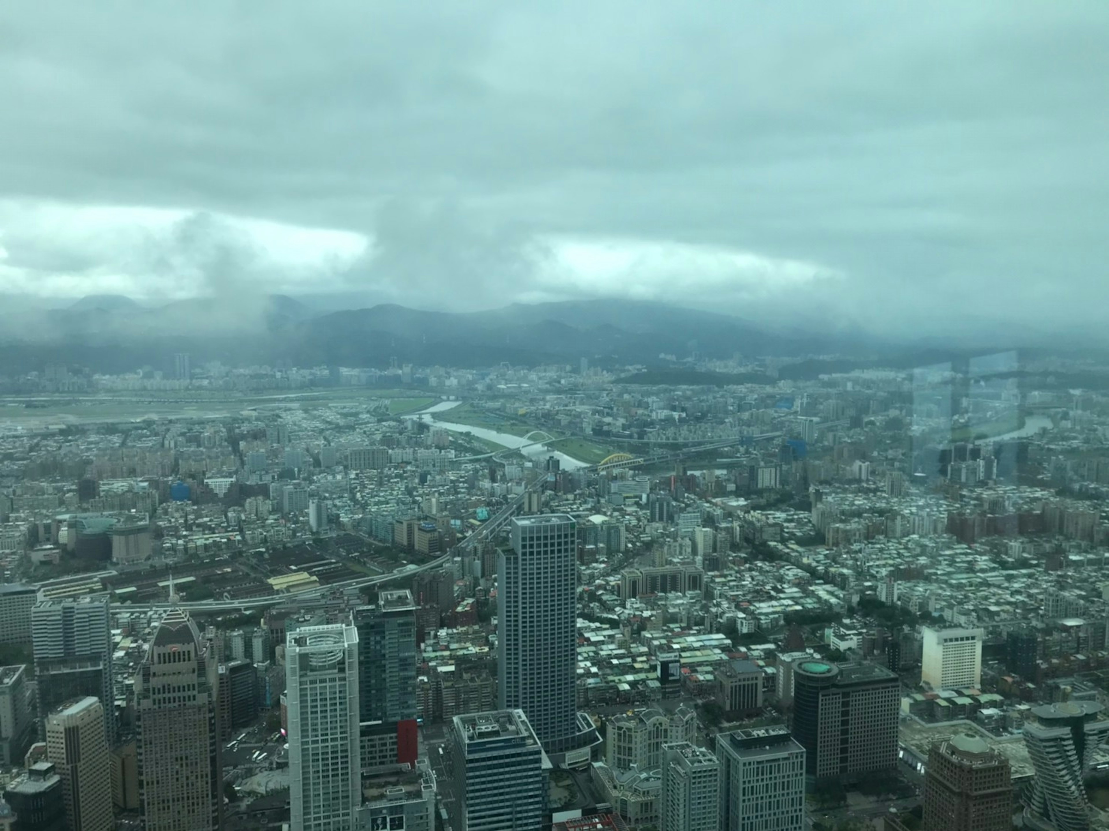 高層ビルと河川を見渡す都市の景観曇り空と山々