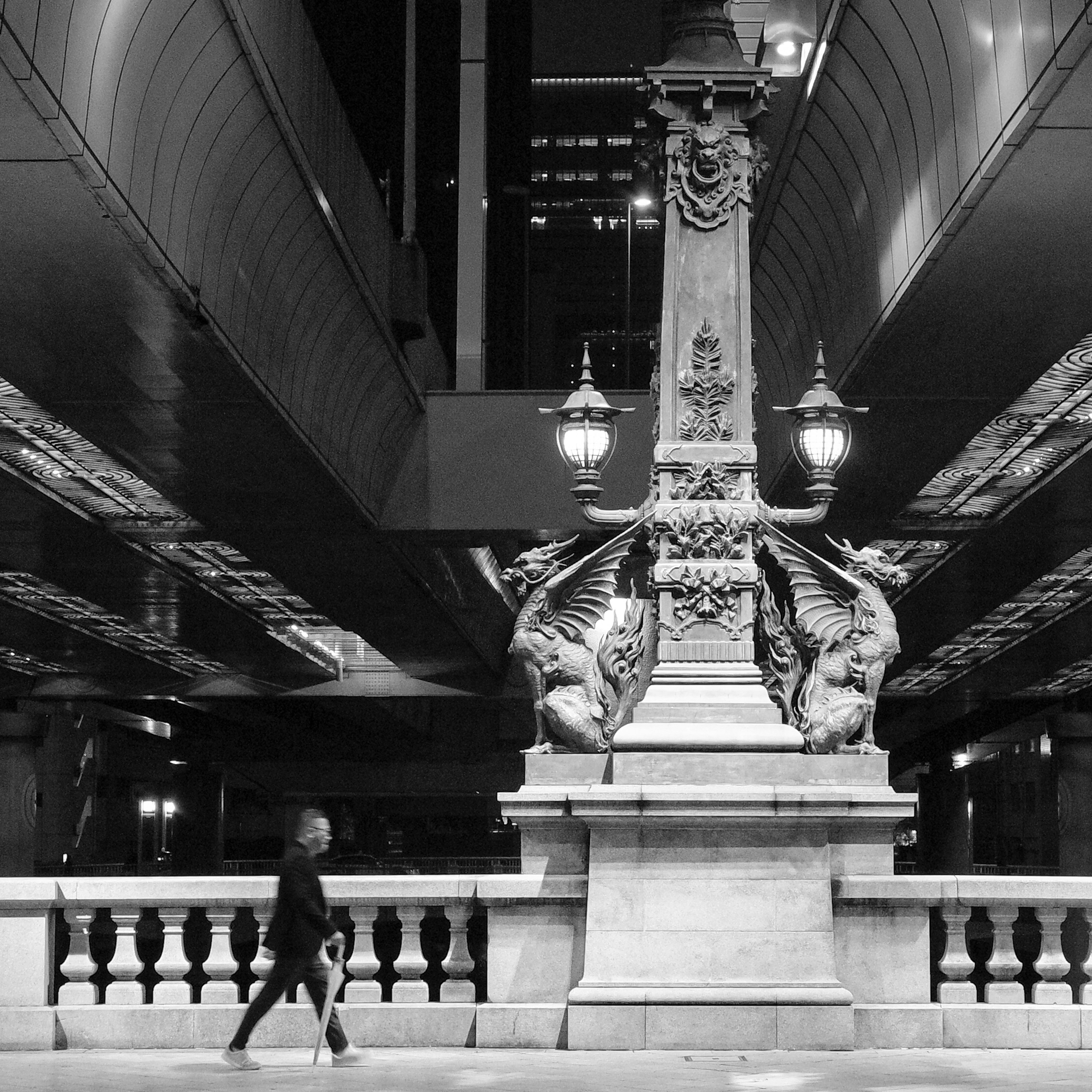 Eine Figur, die nachts durch eine Stadt neben einer dekorativen Säule mit Beleuchtung geht