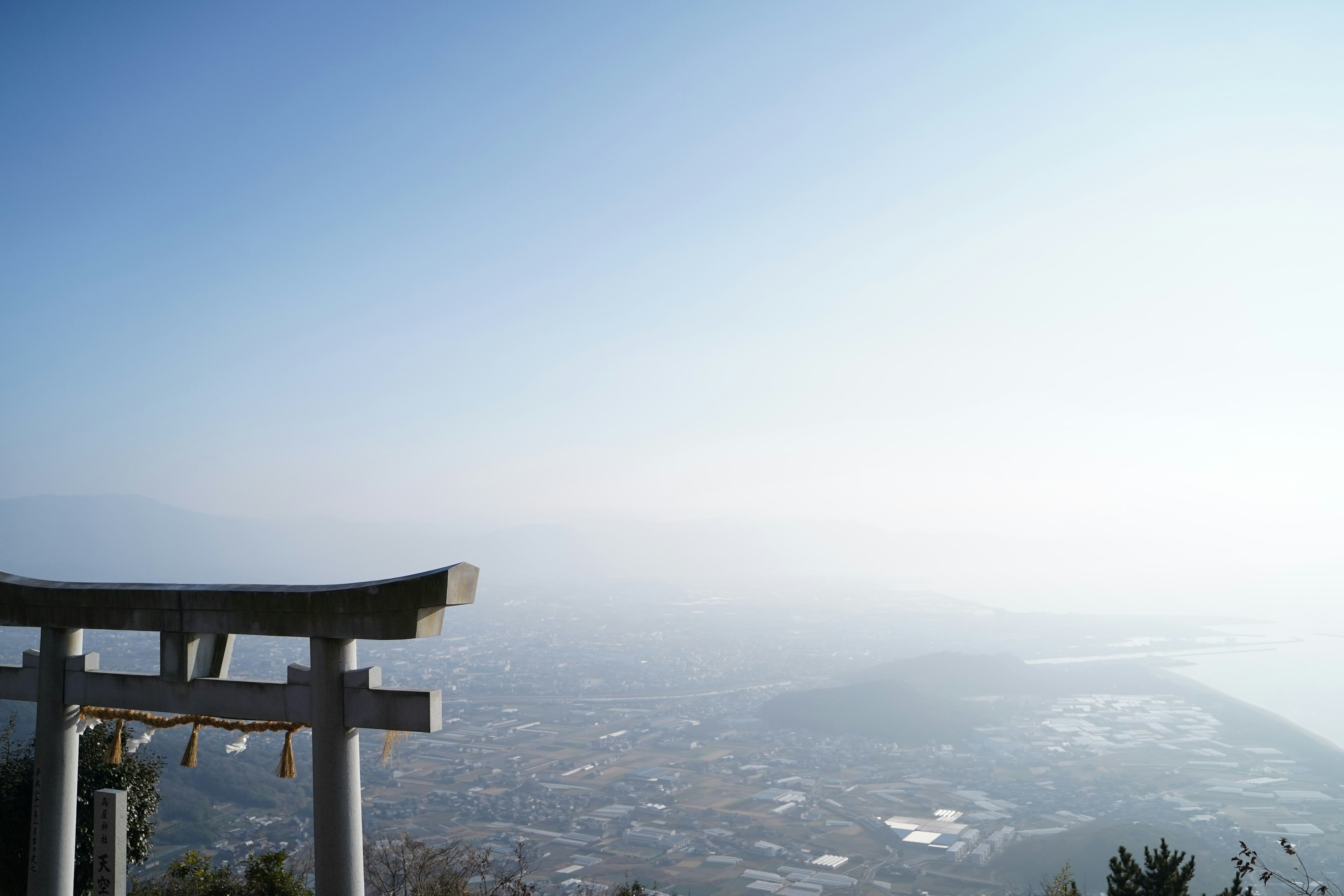 Ein Torii überblickt eine neblige Landschaft unter einem blauen Himmel