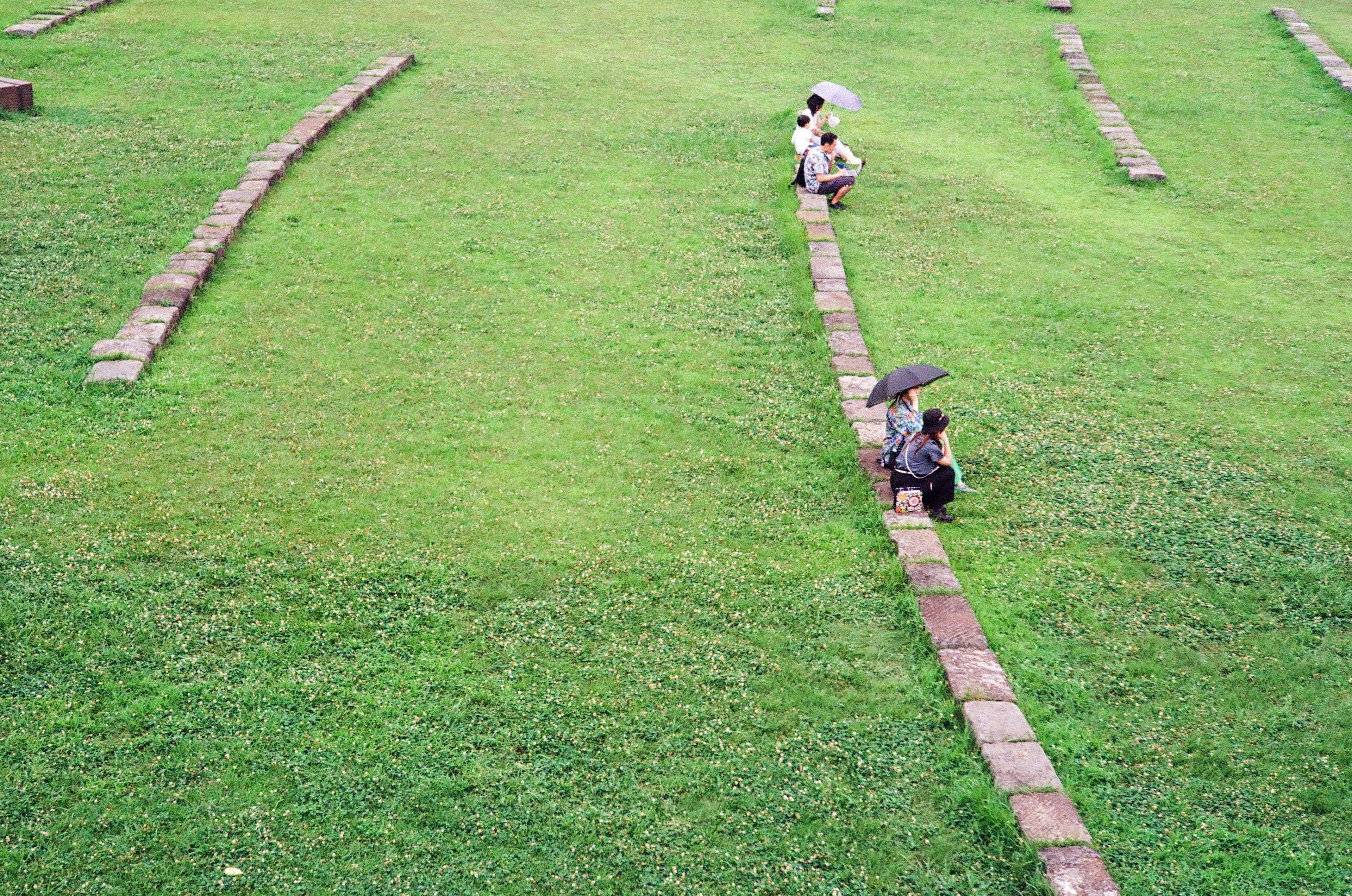 Personas caminando por un camino de piedra en un campo verde con paraguas