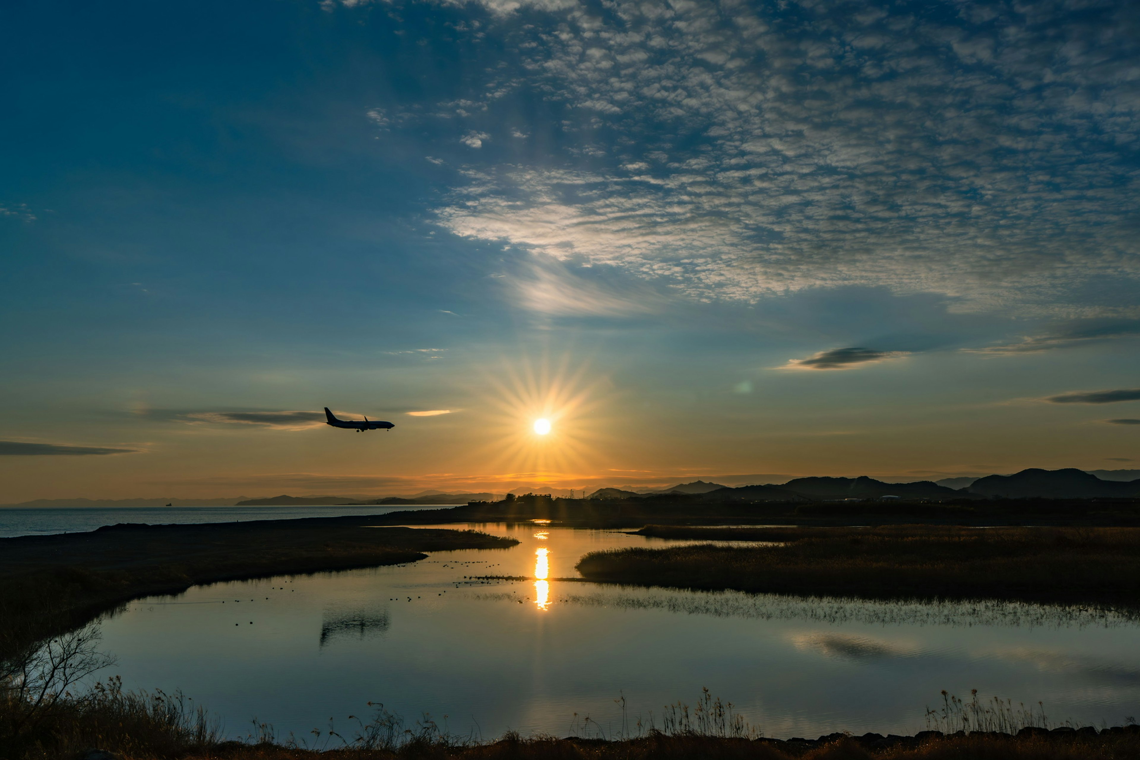 Scenic sunset reflecting on calm water with an airplane flying