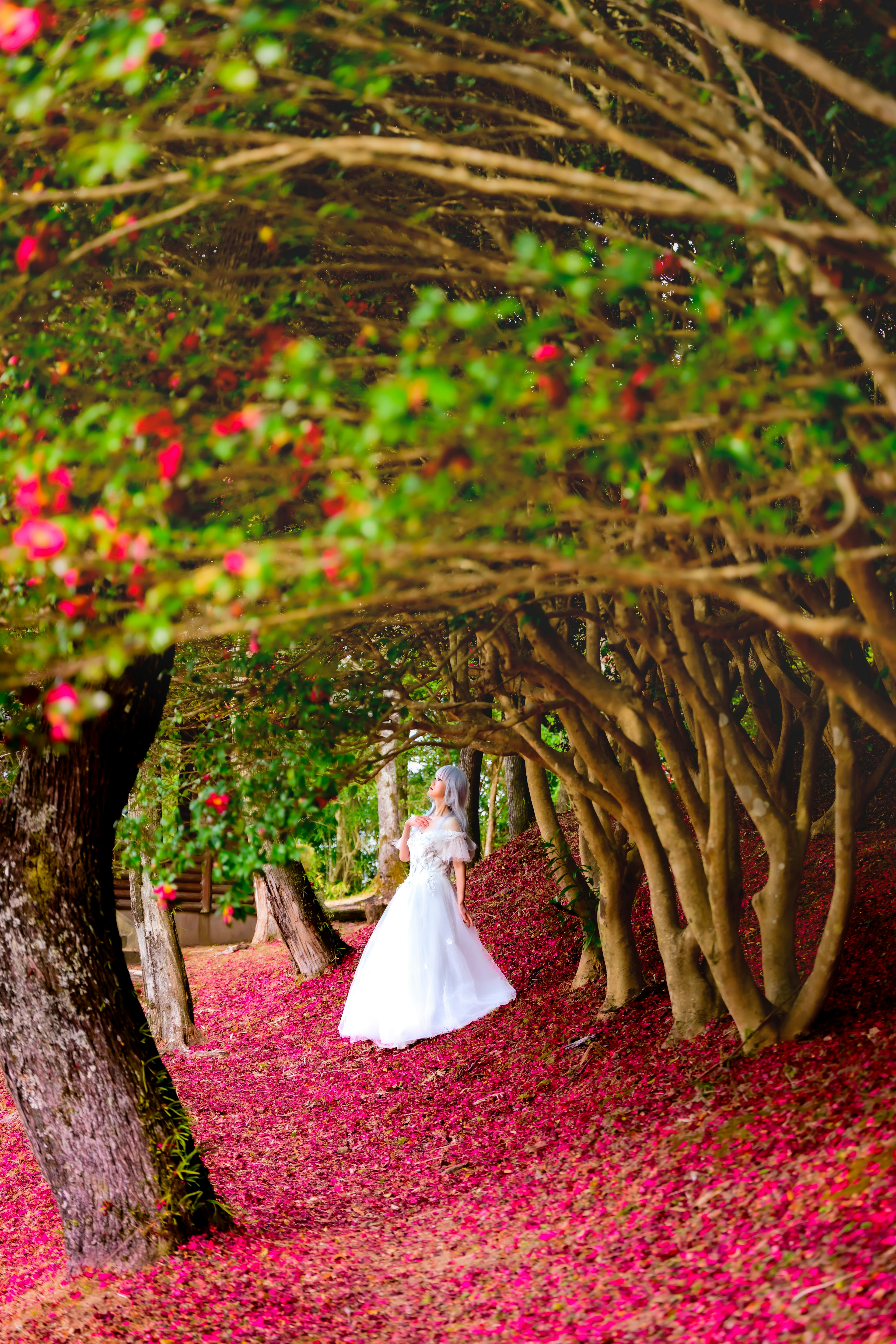 A woman in a white dress walking along a path covered with flower petals