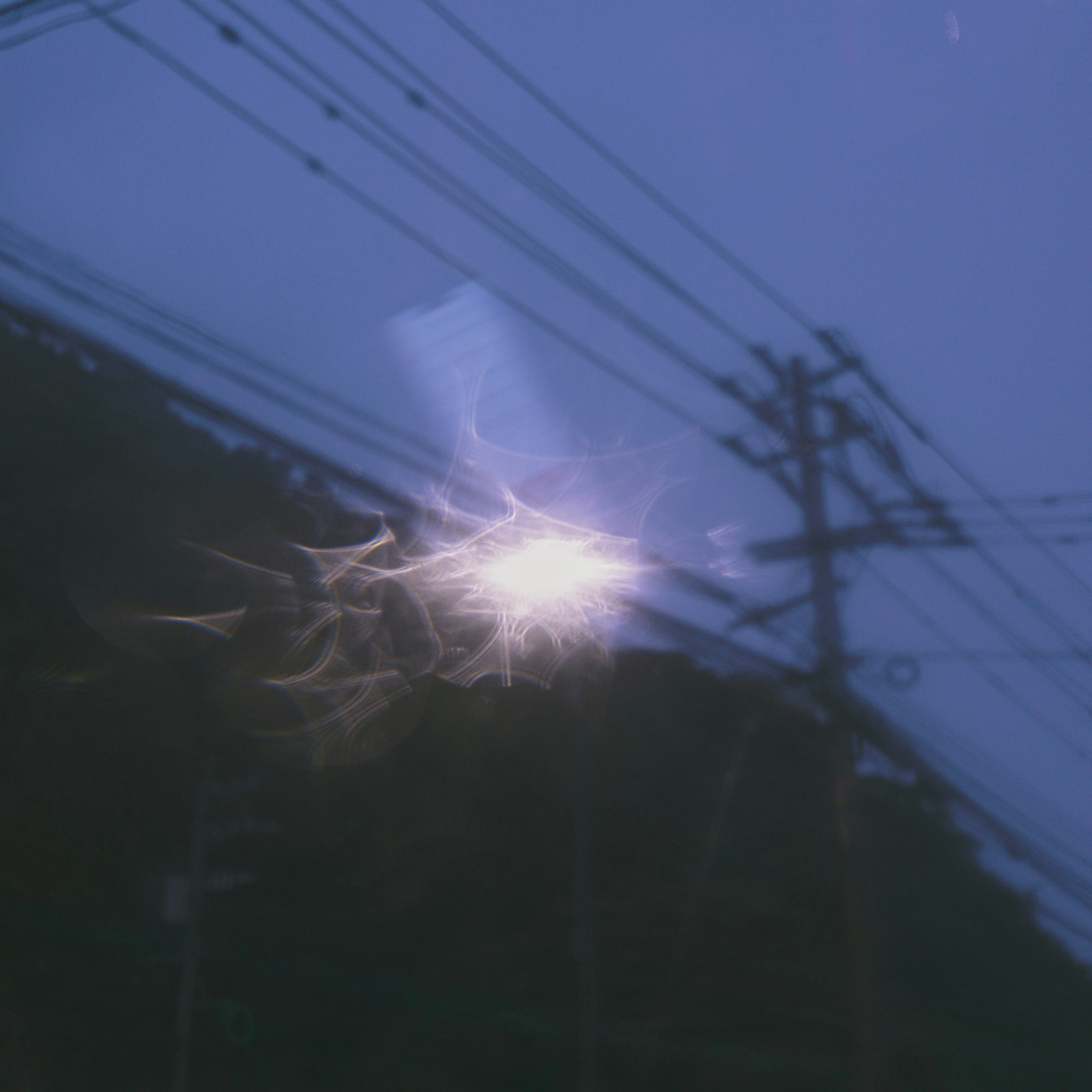 A mystical light reflecting on utility poles and wires against a dark night sky