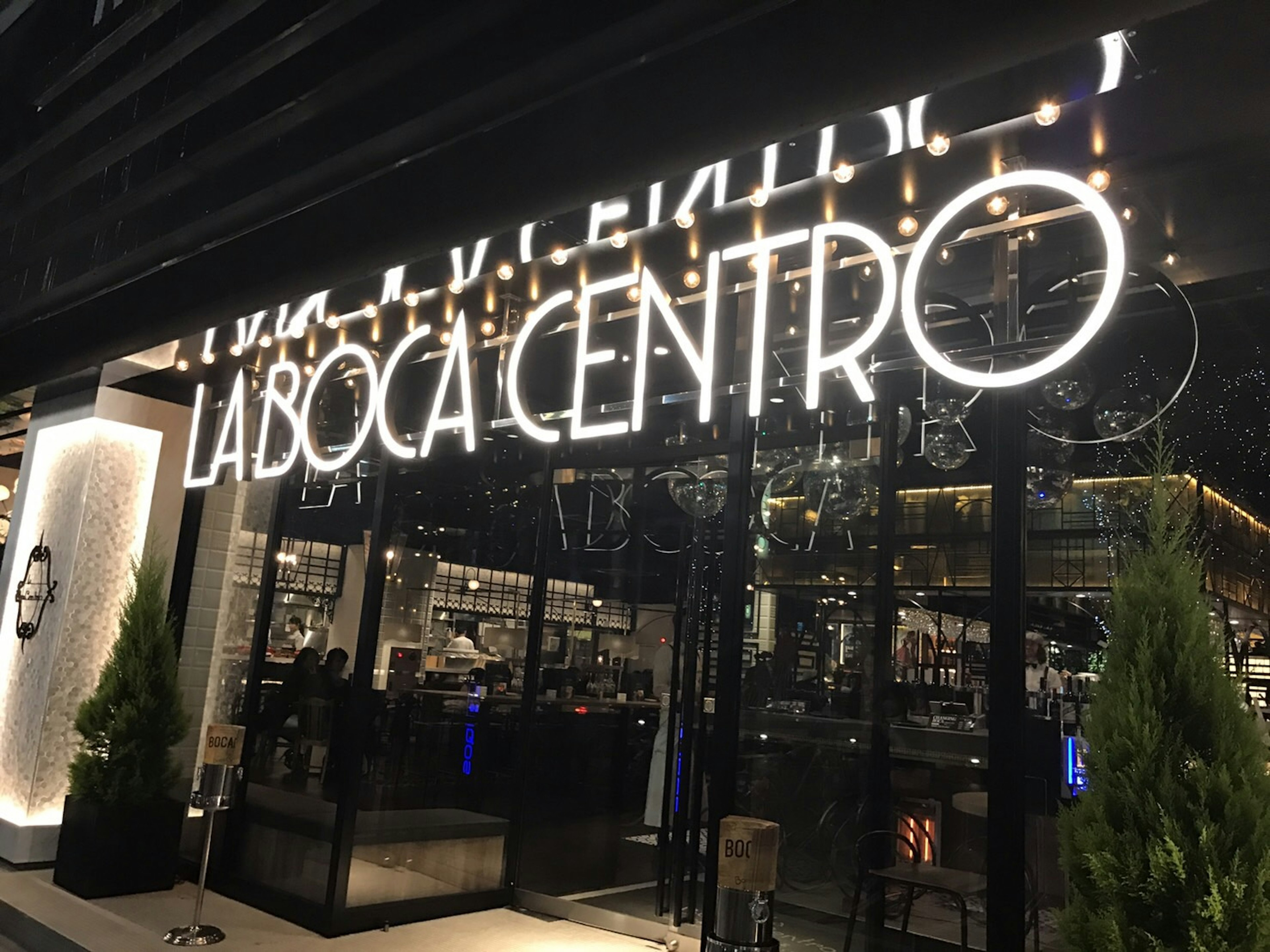 Extérieur moderne de restaurant avec enseigne au néon La Boca Centro et plantes à l'entrée