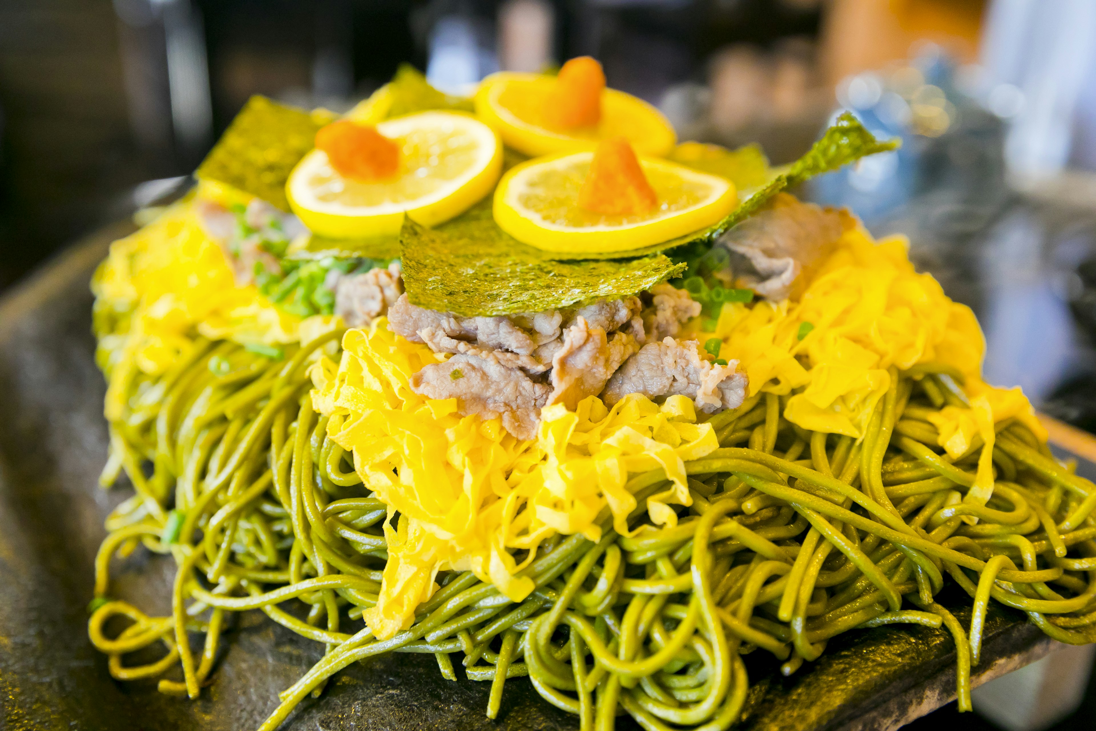 A vibrant dish featuring green noodles topped with yellow egg shavings and slices of lemon