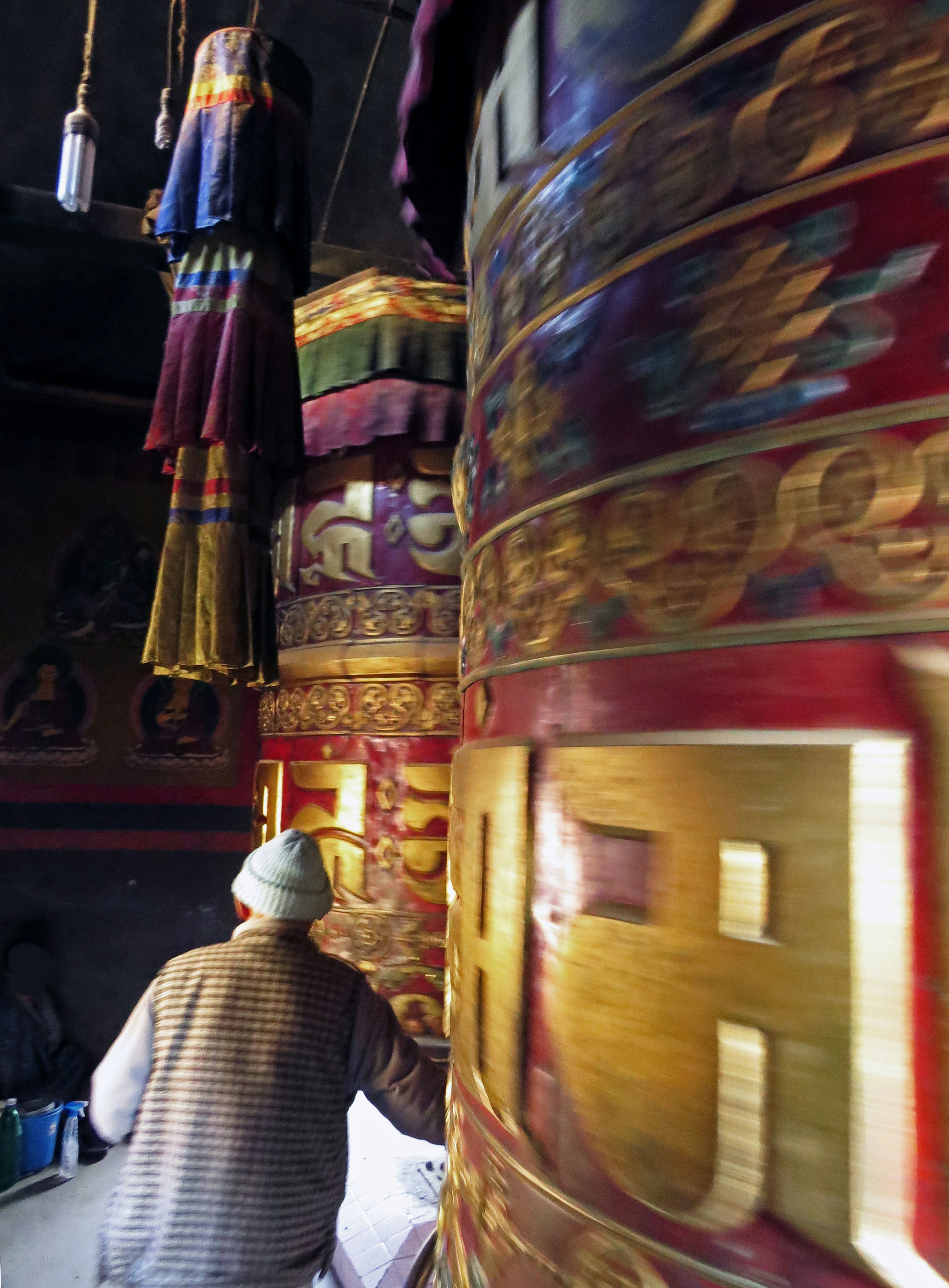 Un moine faisant tourner des moulins à prières avec des couleurs vives et des motifs complexes